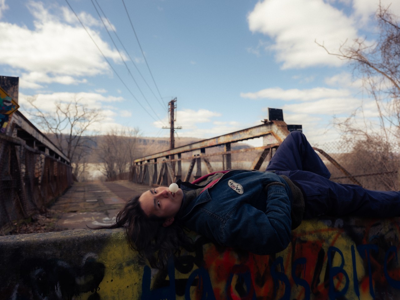 A young Asian American man lies down on a bridge while looking at the camera