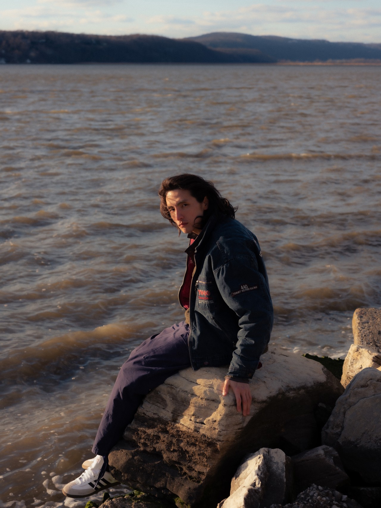 A young Asian-American man sits on a rock overlooking the ocean.