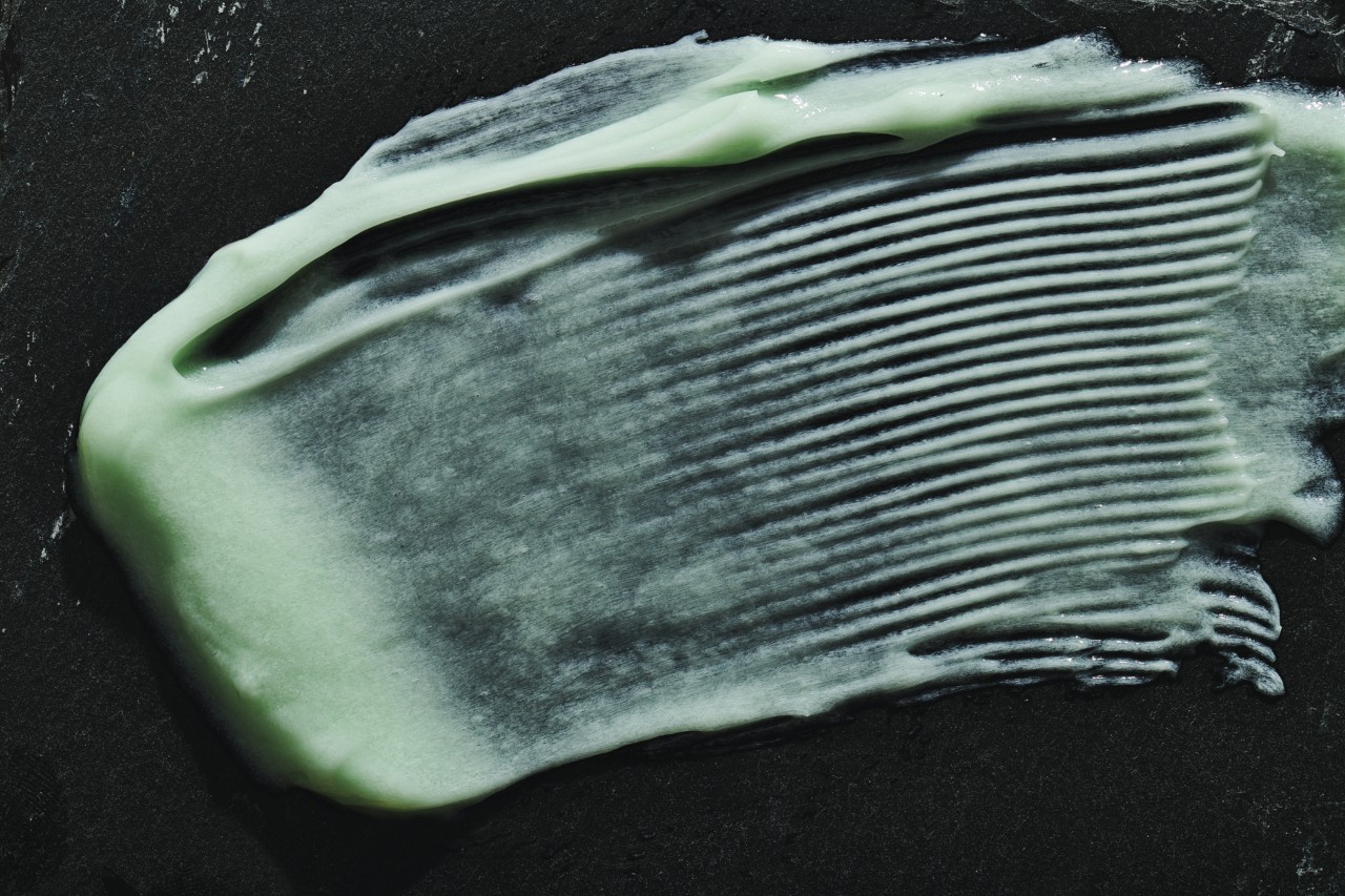 Bright green liquid makeup is smeared against a black background.
