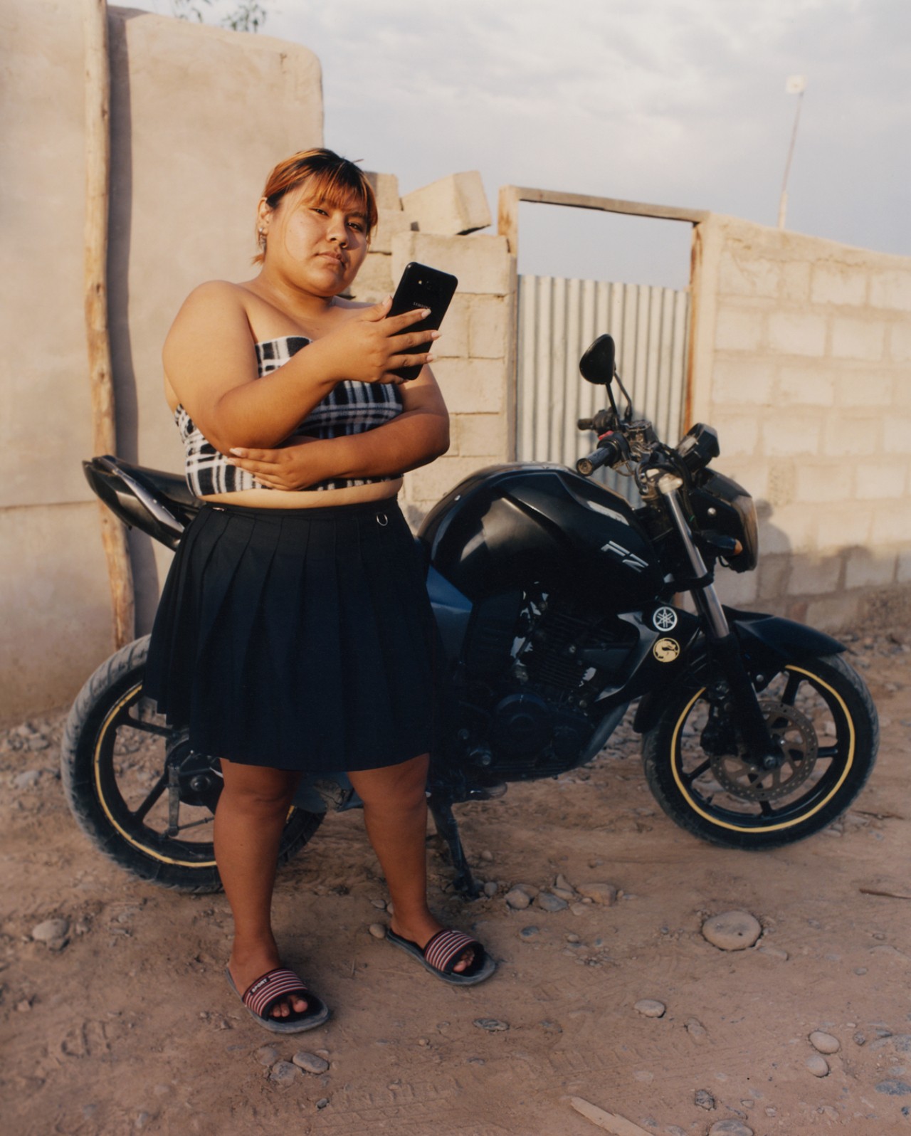 Girl with her phone, standing in front of a motorcycle.