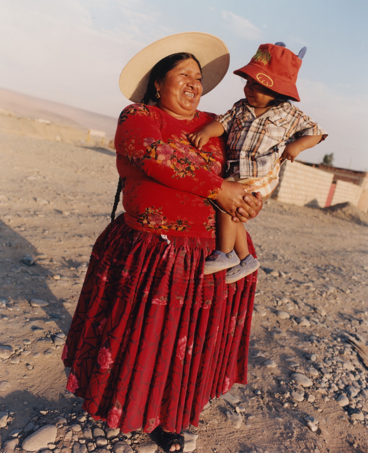 A woman wearing a red pollera, carrying a young child.