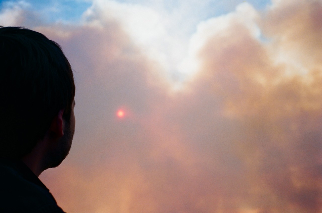 A boy looks up at the cloudy, hazy colored sky.