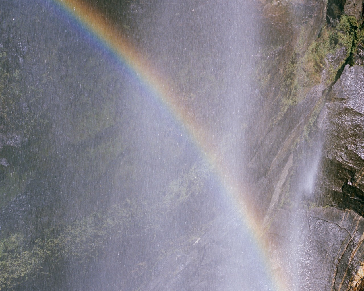 A faint rainbow shines in the light of a waterfall.