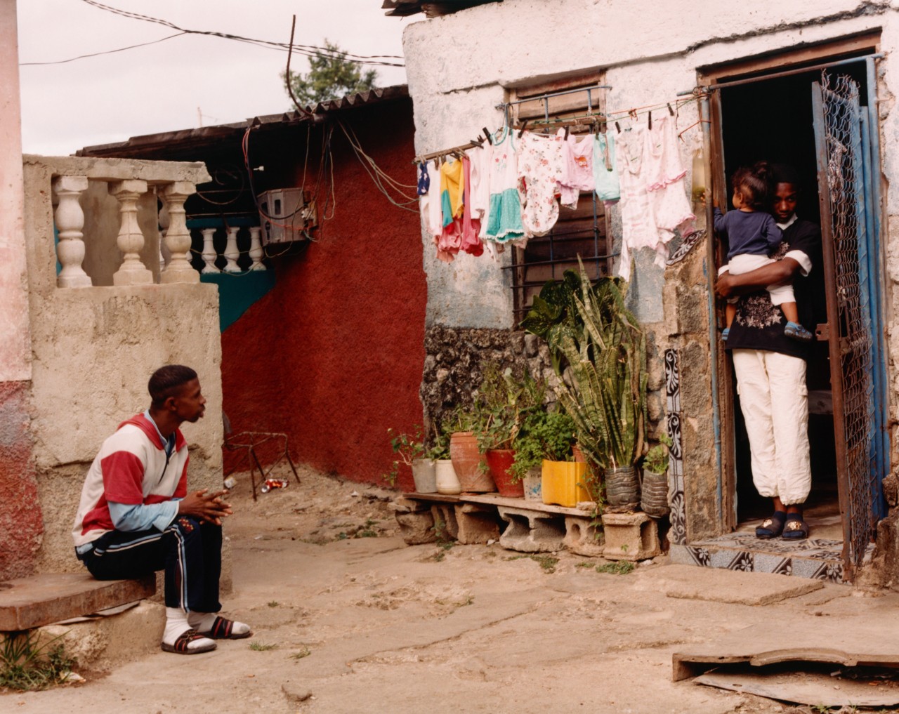 Two men and a small child are in the backyard of a Cuban home.