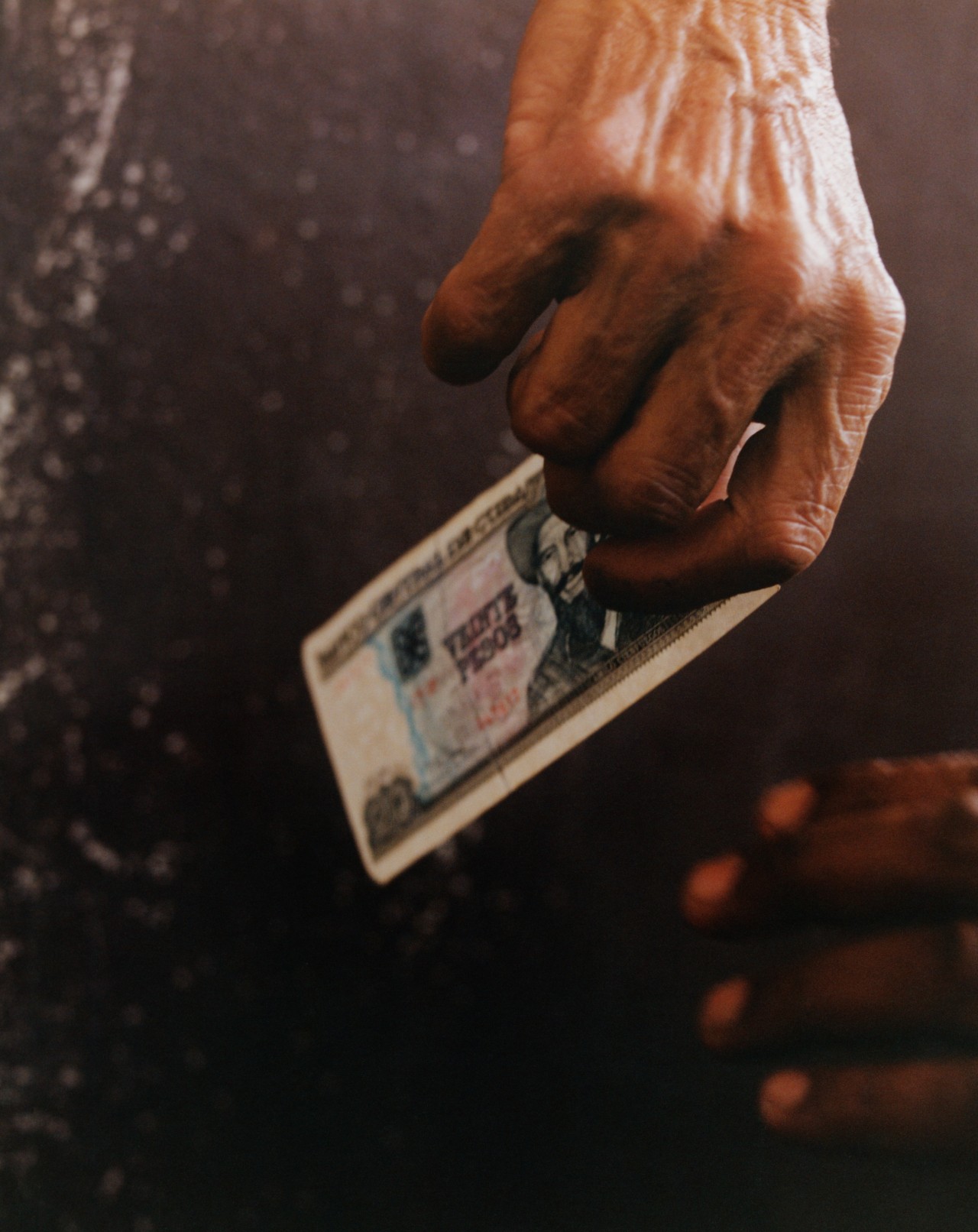 An older person's hand holds a 20 dollar Cuban bill.