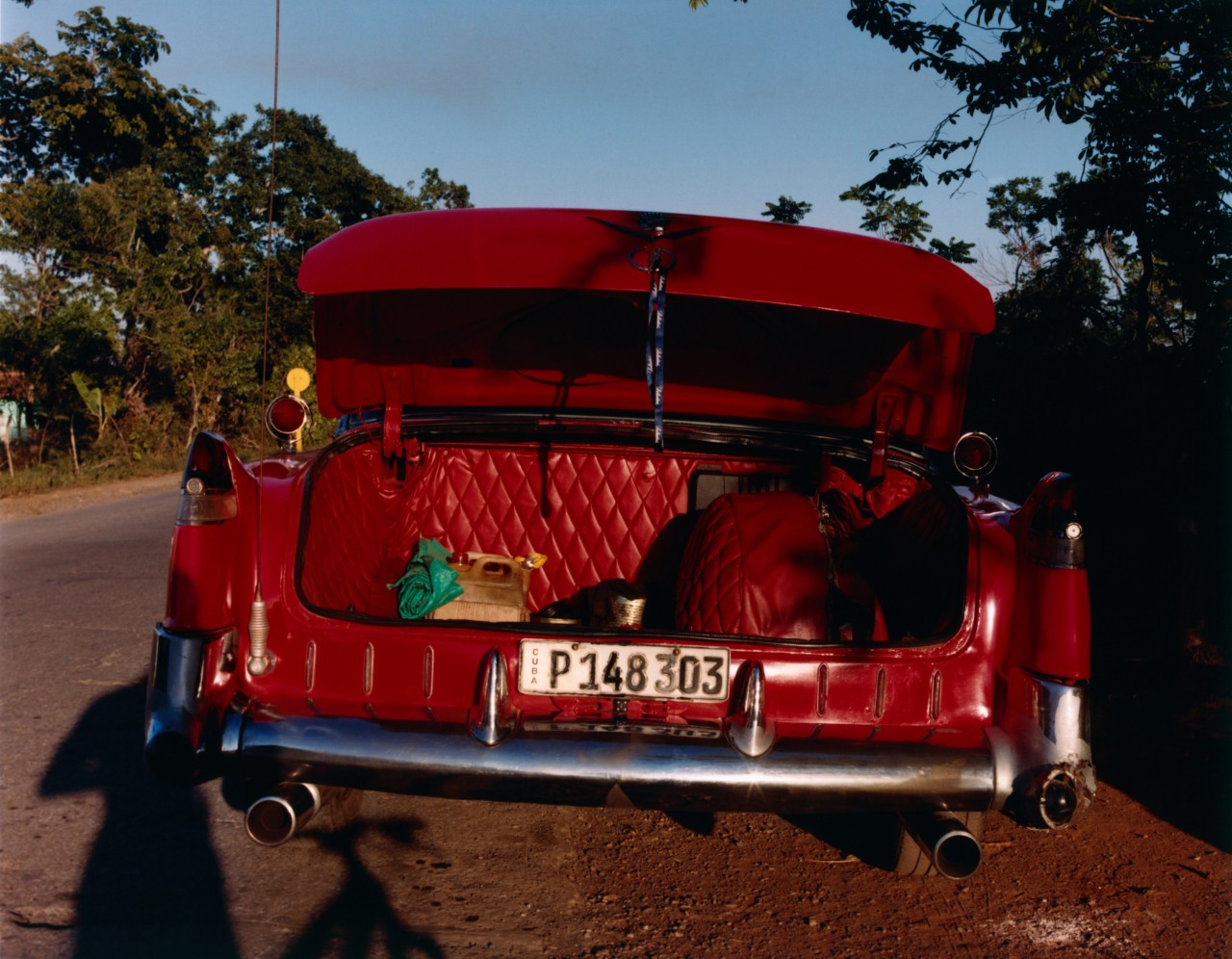 The trunk of a bright red car is wide open on the side of a street in Cuba.