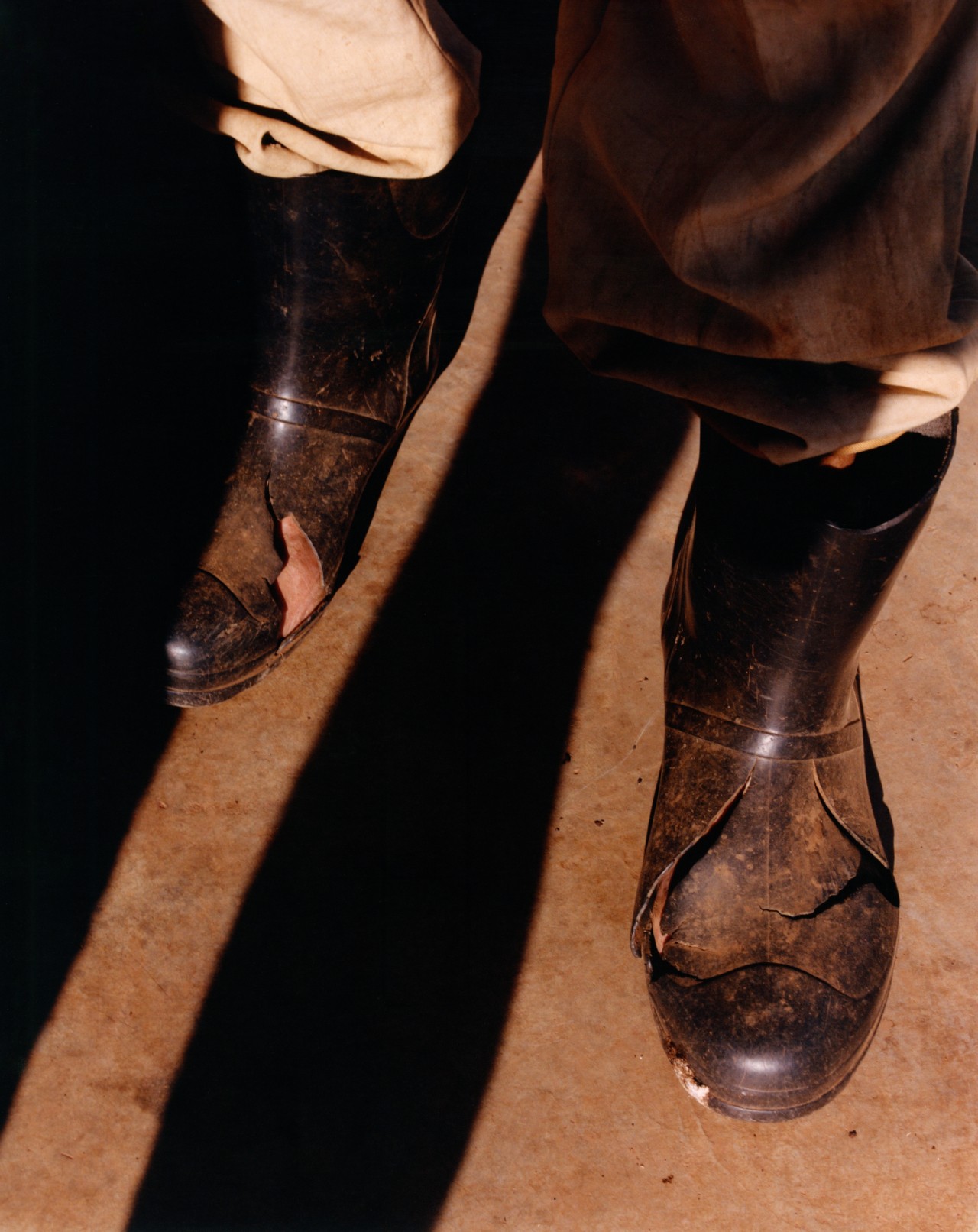 A pair of feet wearing large black boots is covered in half sunlight half shadows on the sidewalk.