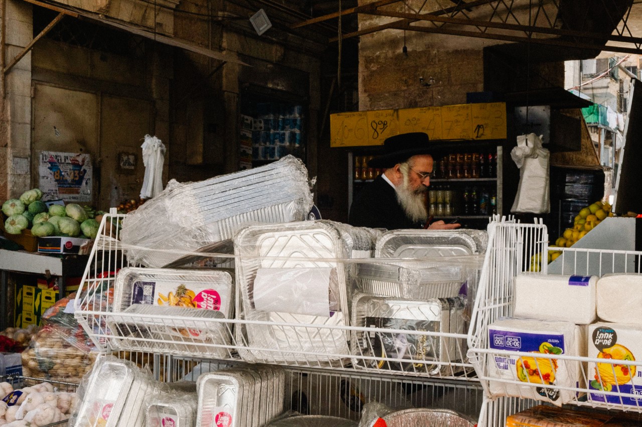 An ultra-Orthodox Jewish man is partially shown standing behind a rack of plastic containers.