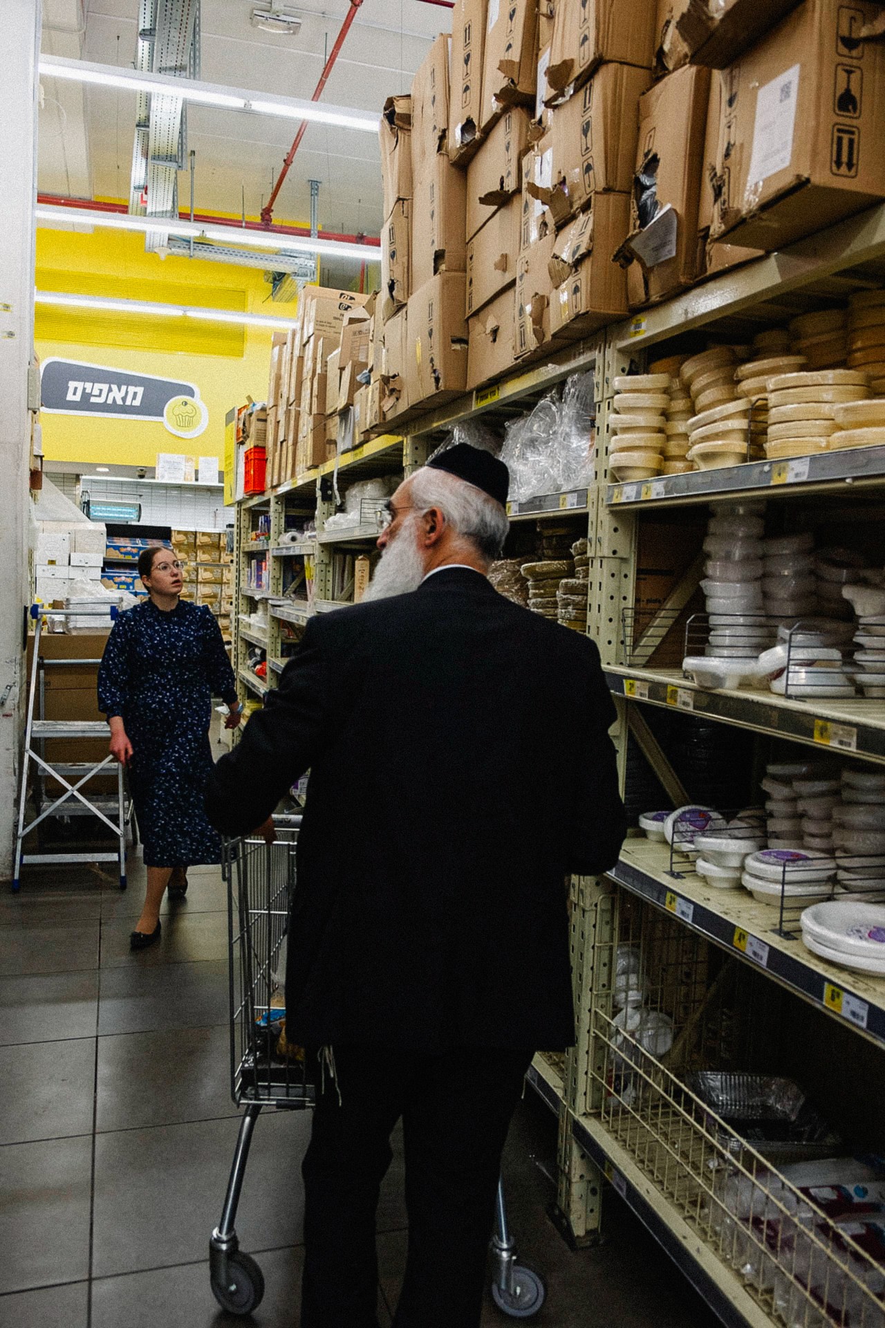 An ultra-Orthodox Jewish man pushes his shopping cart through the plastics aisle of the grocery store.