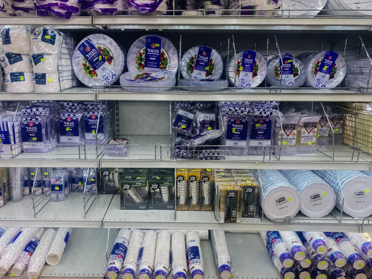 The plastics section of a grocery store displays plates, utensils, cups, and other materials.