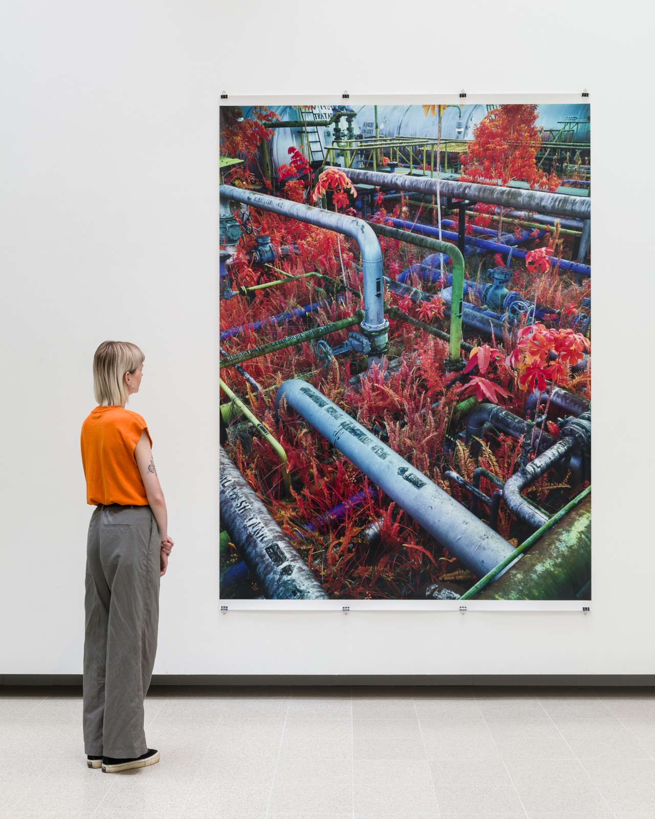 A woman dressed in an orange shirt faces away from the camera, looking at a large painting hanging on a white wall at the Hayward Gallery.
