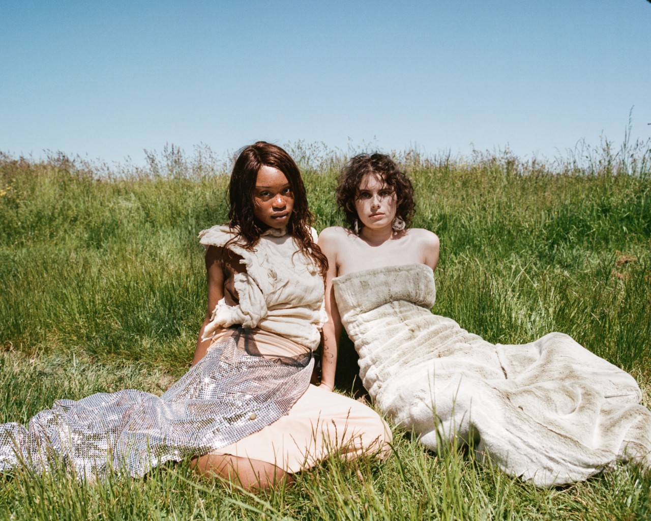 Two models wearing Ponte brand clothing are sitting next to each other in a field of grass.