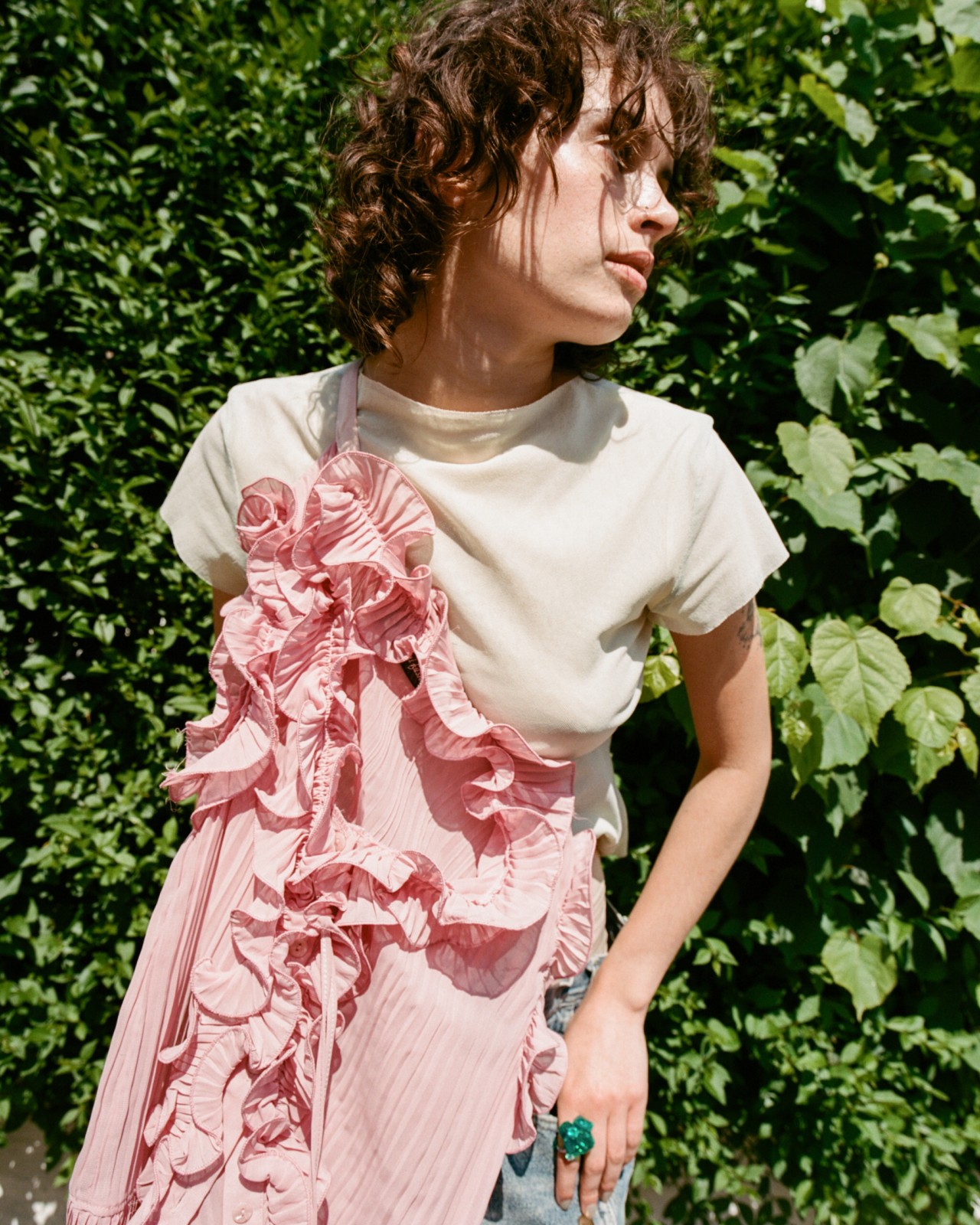 A model wearing Ponte brand looks to the side while posing in front of a large green bush.