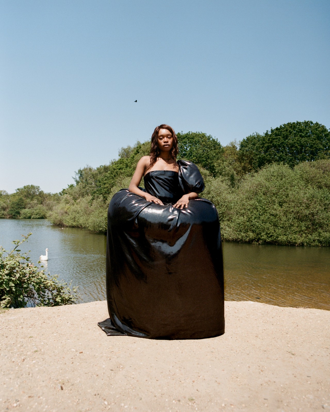 A model wearing a large black garment stands in front of a large lake.