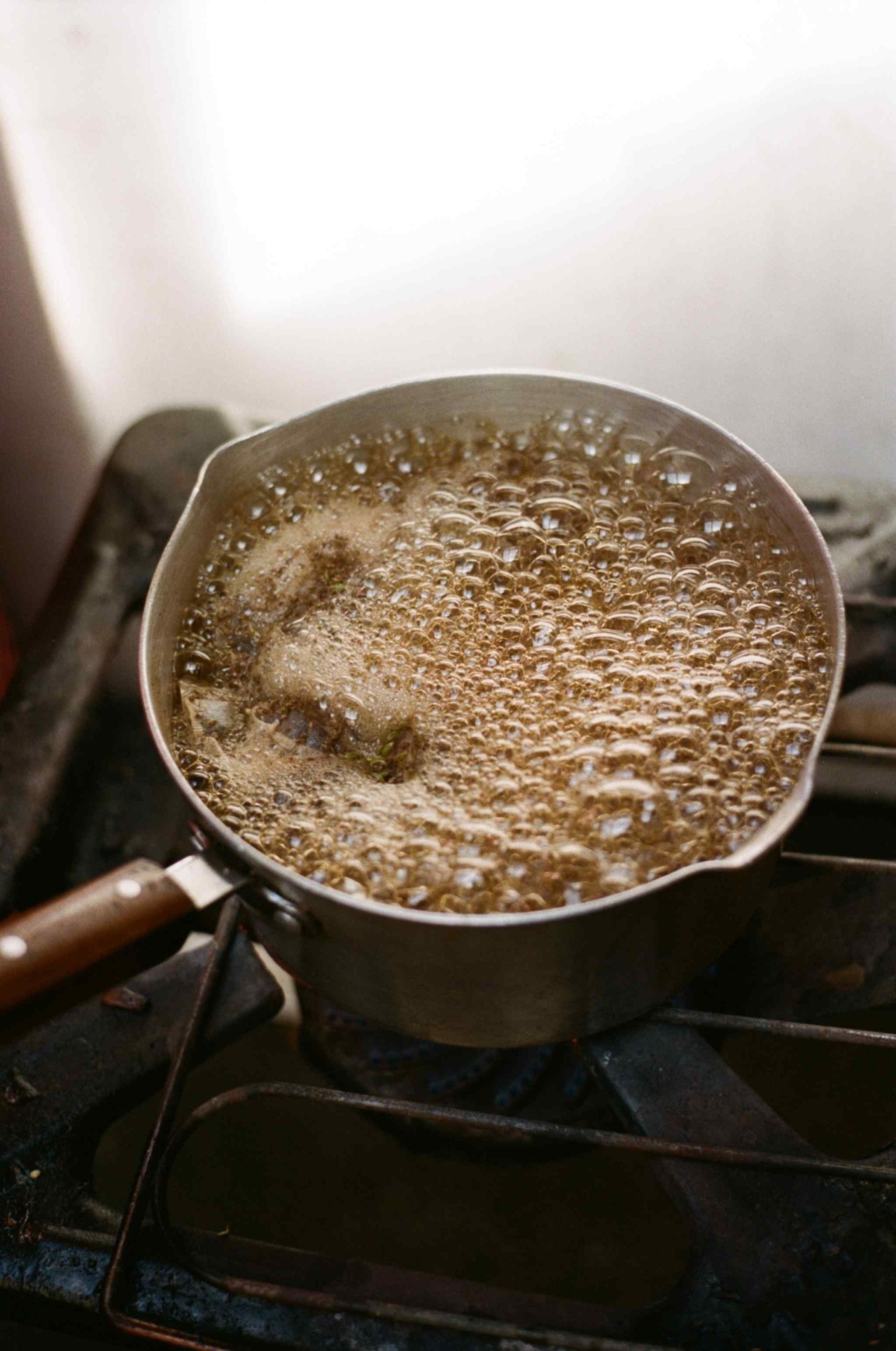 A brown liquid boils in a small pot on a stove.
