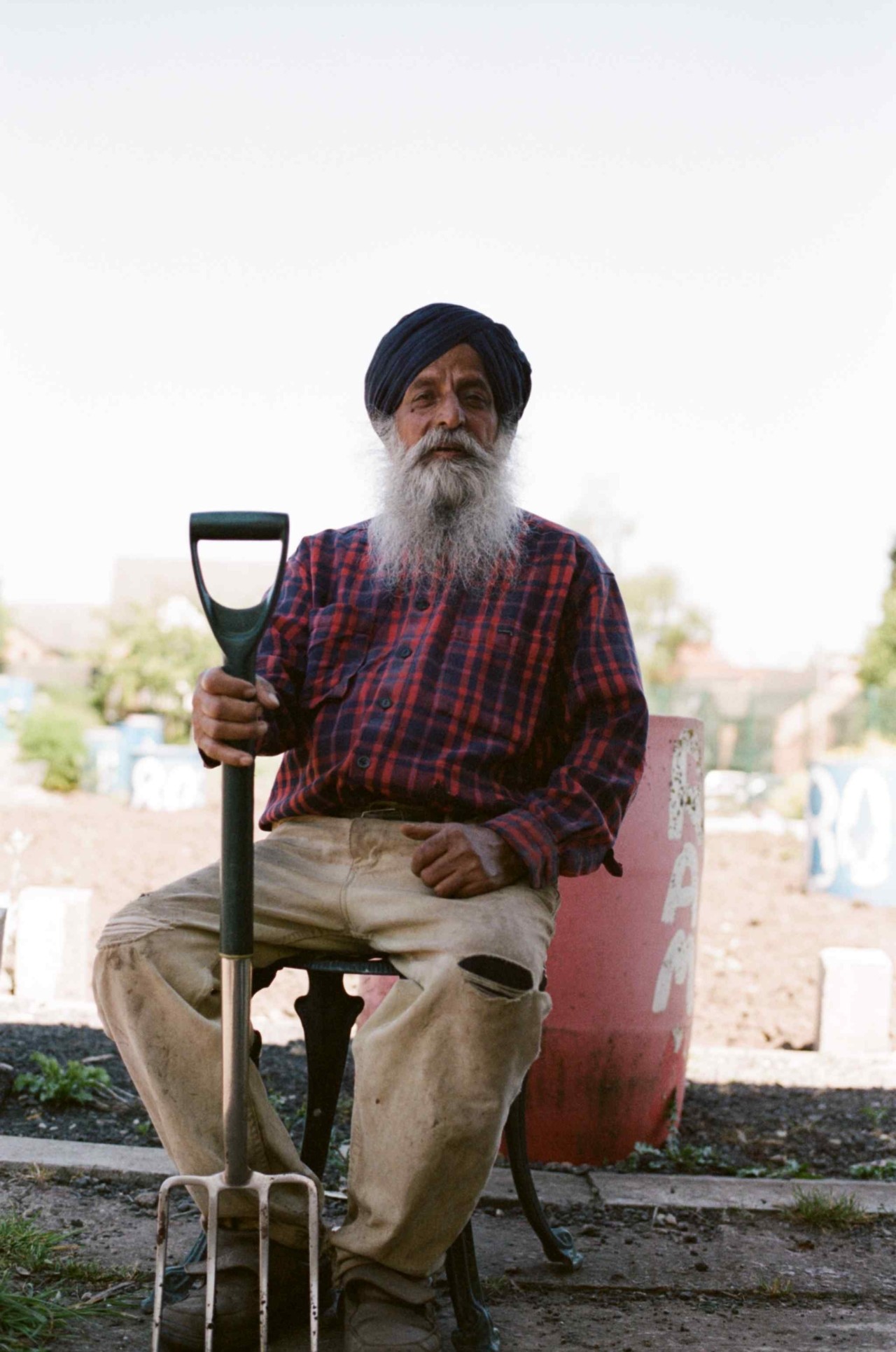 A Punjabi Sikh farmer sits down with a gardening tool in his hand.