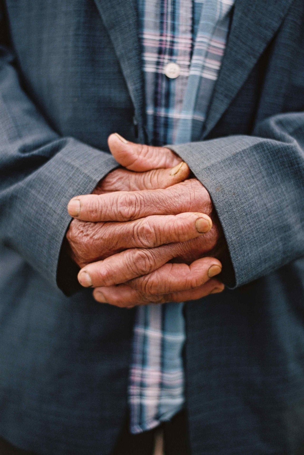 The hands of a farmer clasps their hands together.