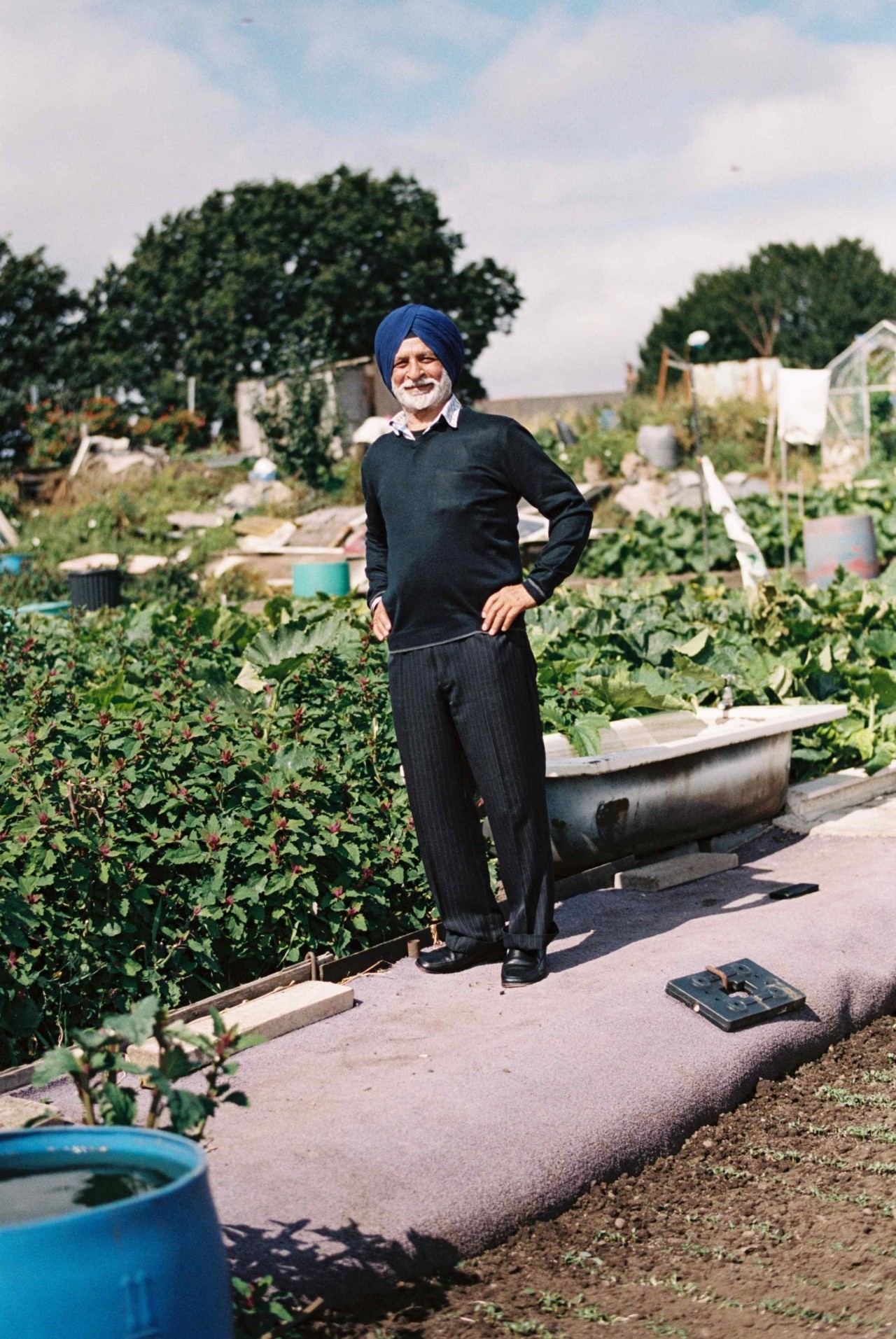 A farmer stands on a tarp with their hands on their hips in front of a farm.