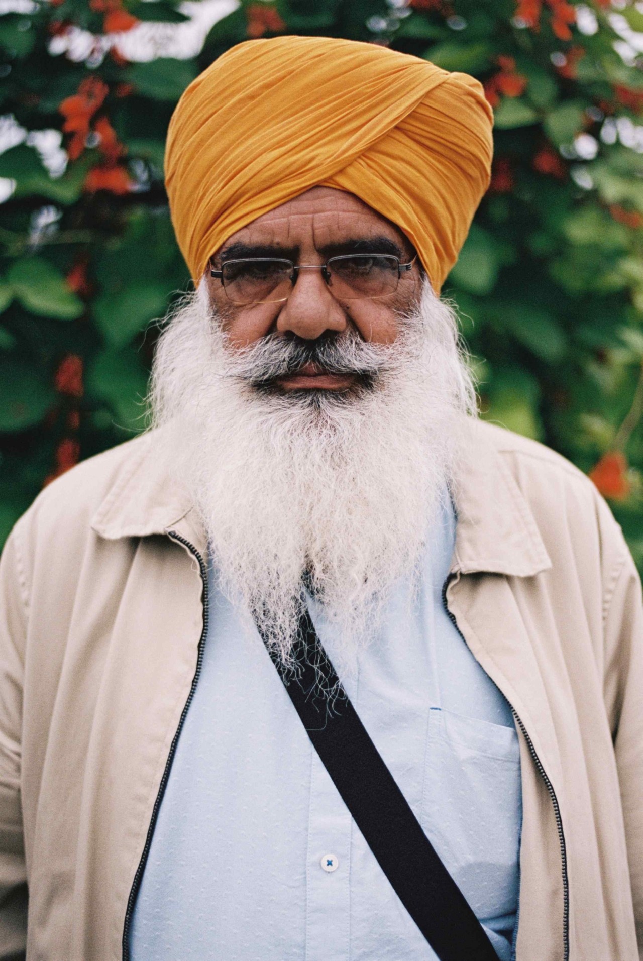 A Punjabi Sikh man with a white beard and a yellow head wrap stares plainly into the camera.