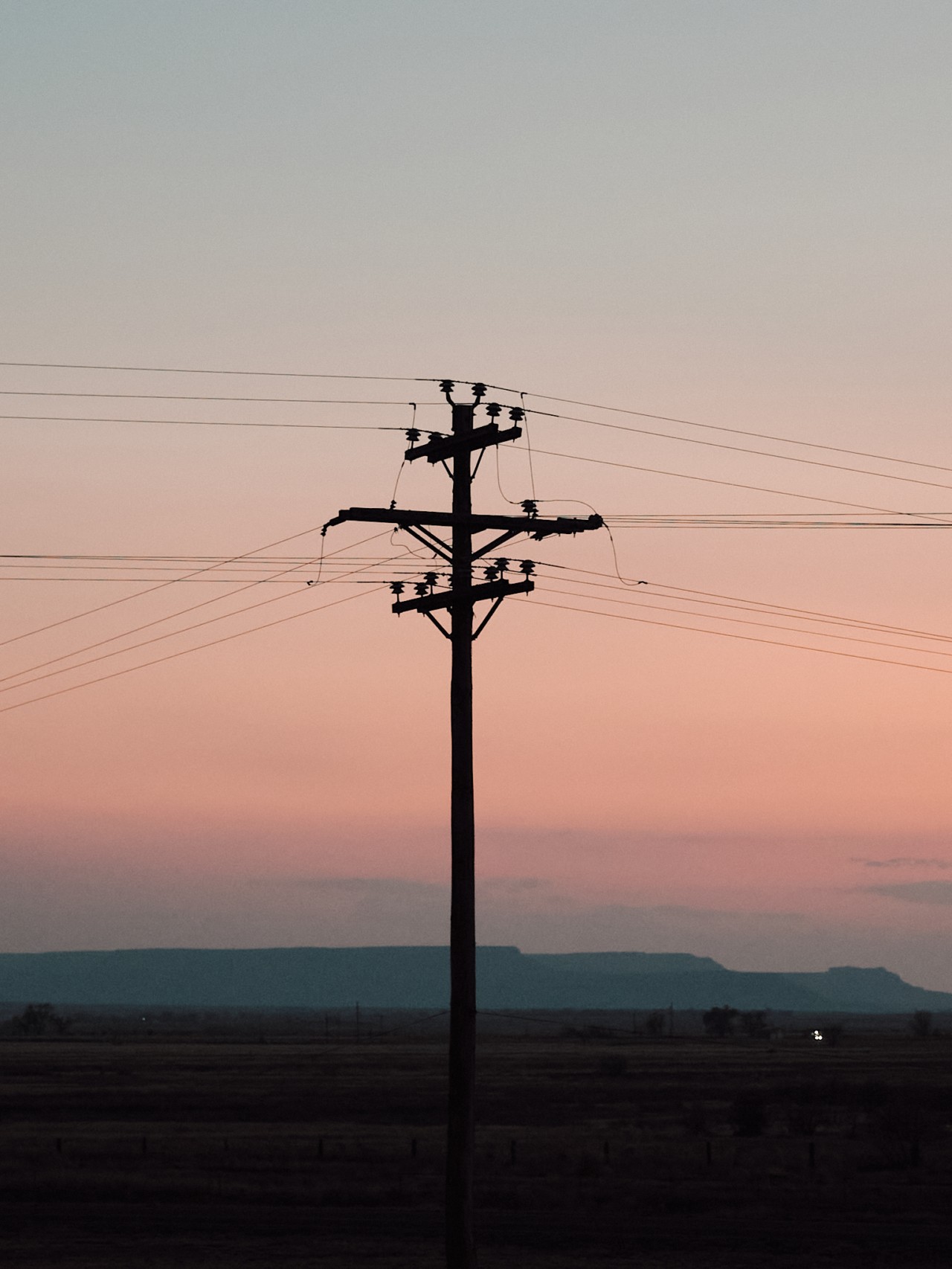 The shadow of a street light stands tall in front of a dusky mountainous horizon.