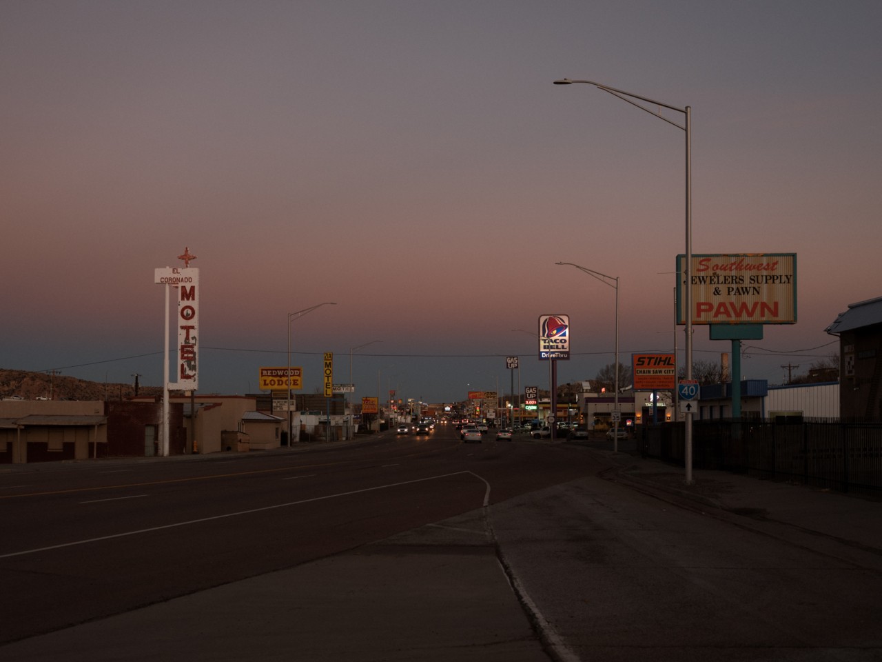 Barren business signs are shown along a street in a ghost town along Route 66. It's dusk.