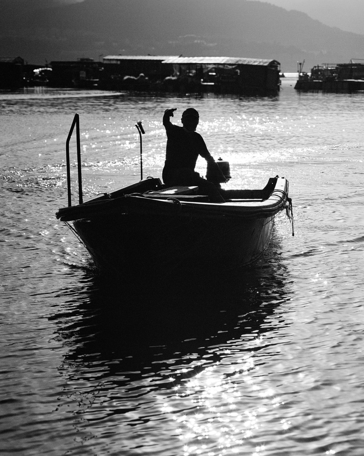 A black and white image of a man floating in a boat, facing away from the camera.