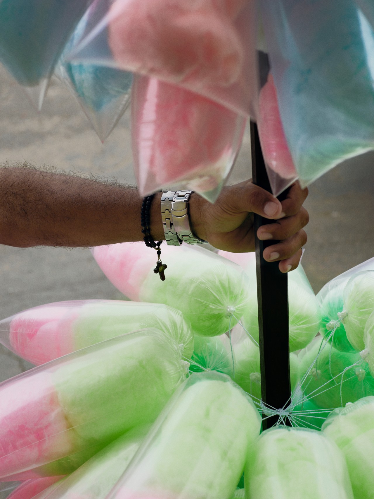 A hand is holding a stick with blue and pink cotton candy attached to it. The stick hovers over an array of even more green and pink cotton candy.