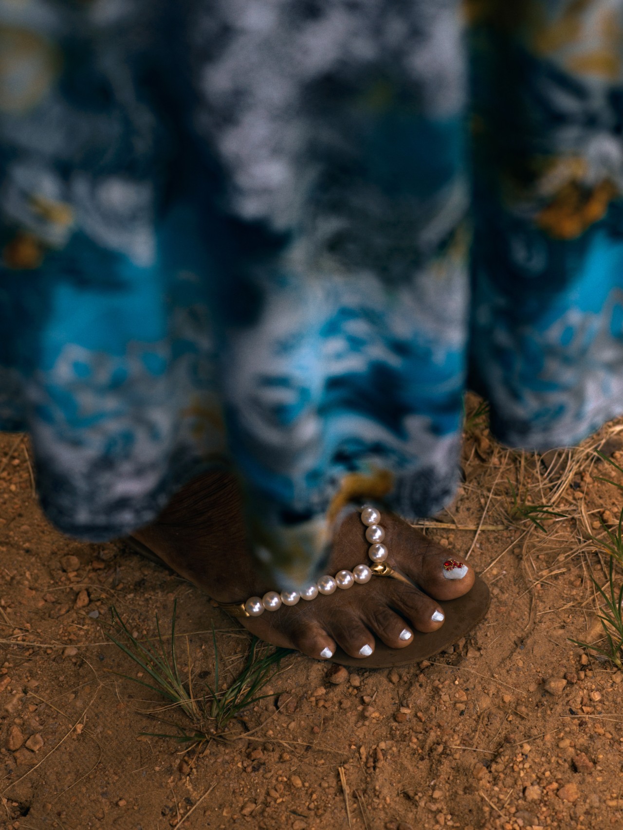 The foot of a person is shown standing on a dirt path in the Amazon rainforest. They are wearing a long dress and a silver flip flop.