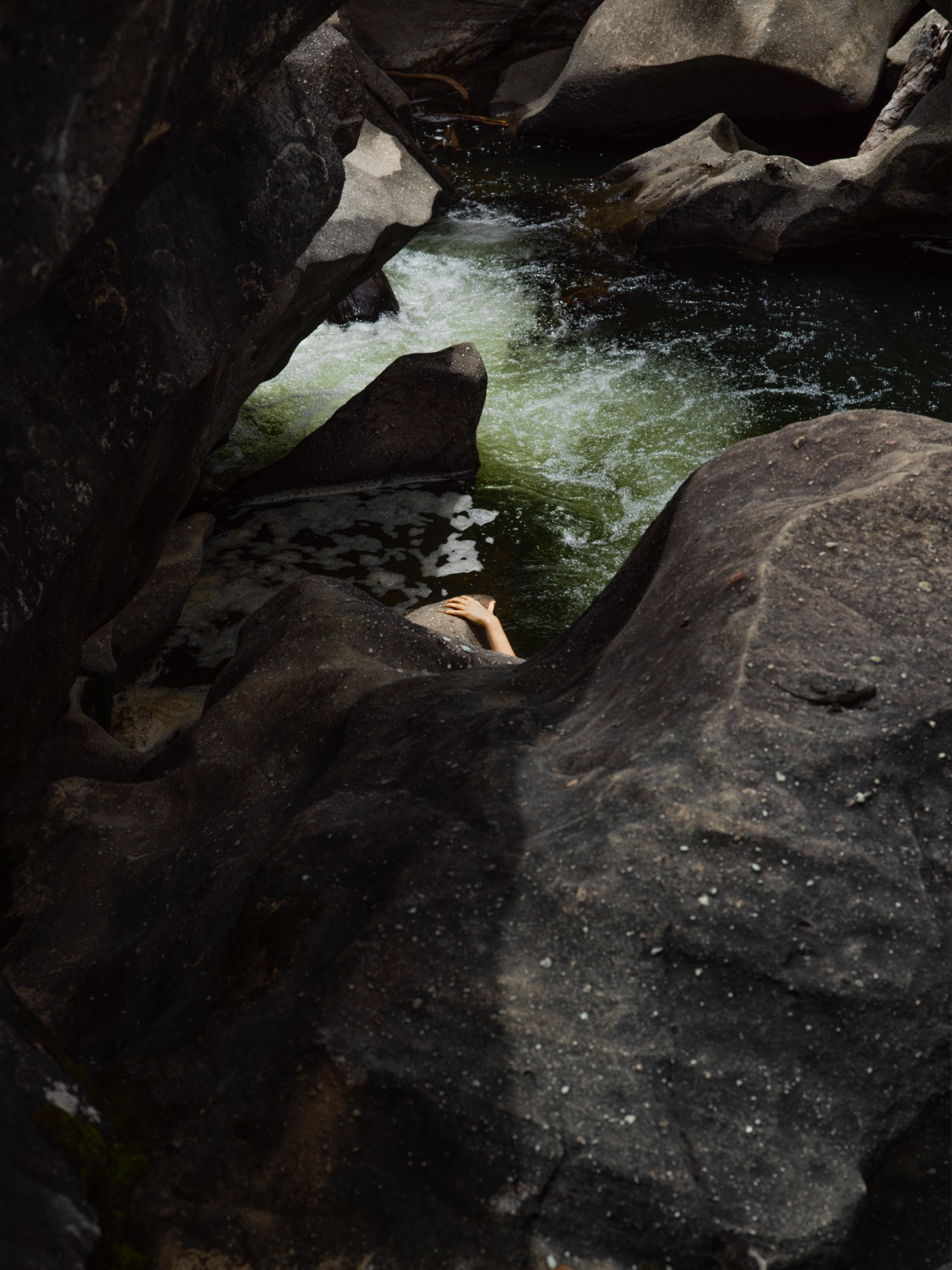 A hand is shown grabbing a rock in the distance of a rocky cave like lagoon in the Amazon rainforest.