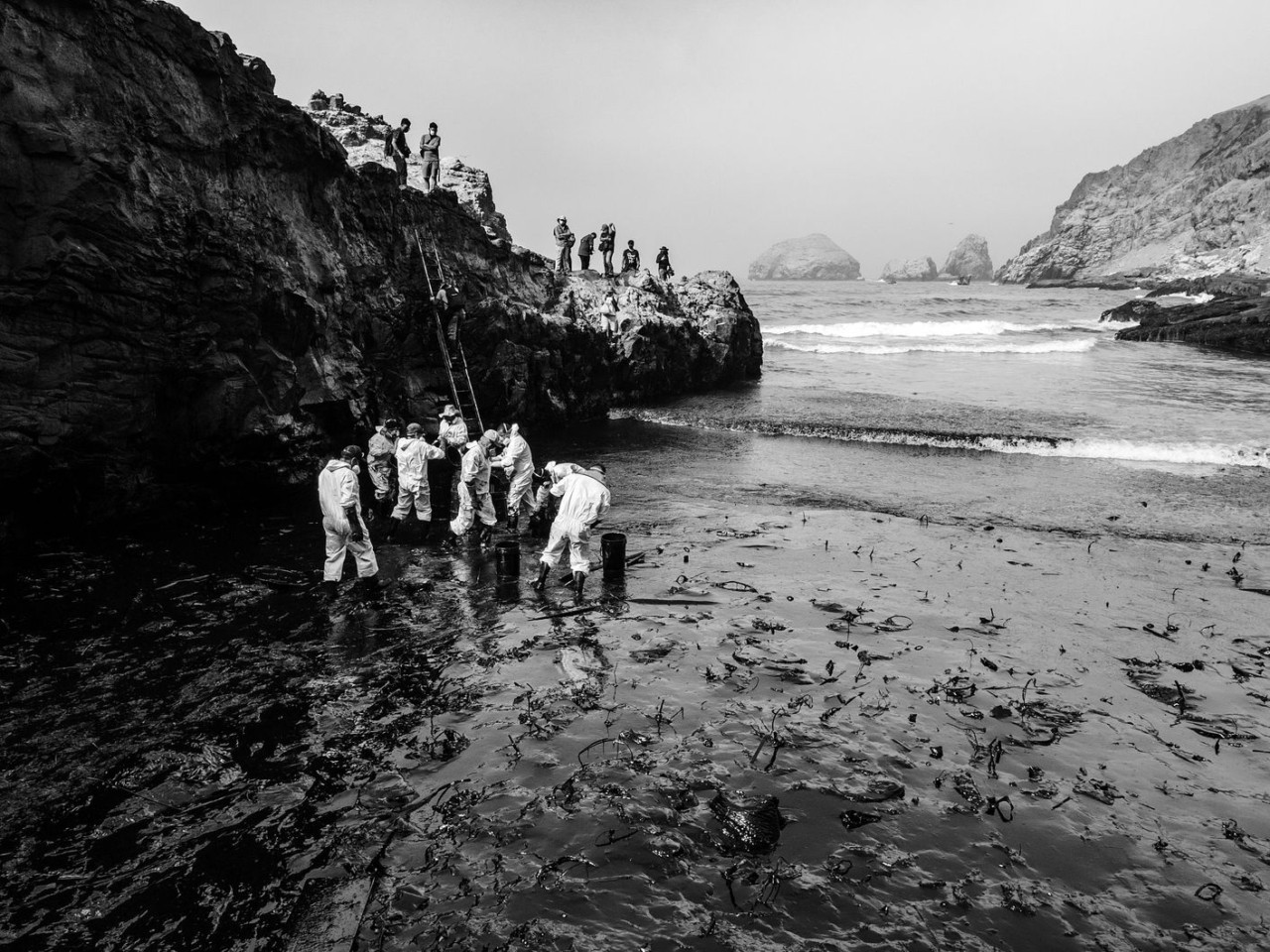 A crew helps clean up a huge oil spill oceanside in Peru.