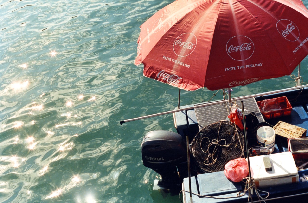 A large red umbrella stands up on a boat floating on the water in a Hong Kong village.