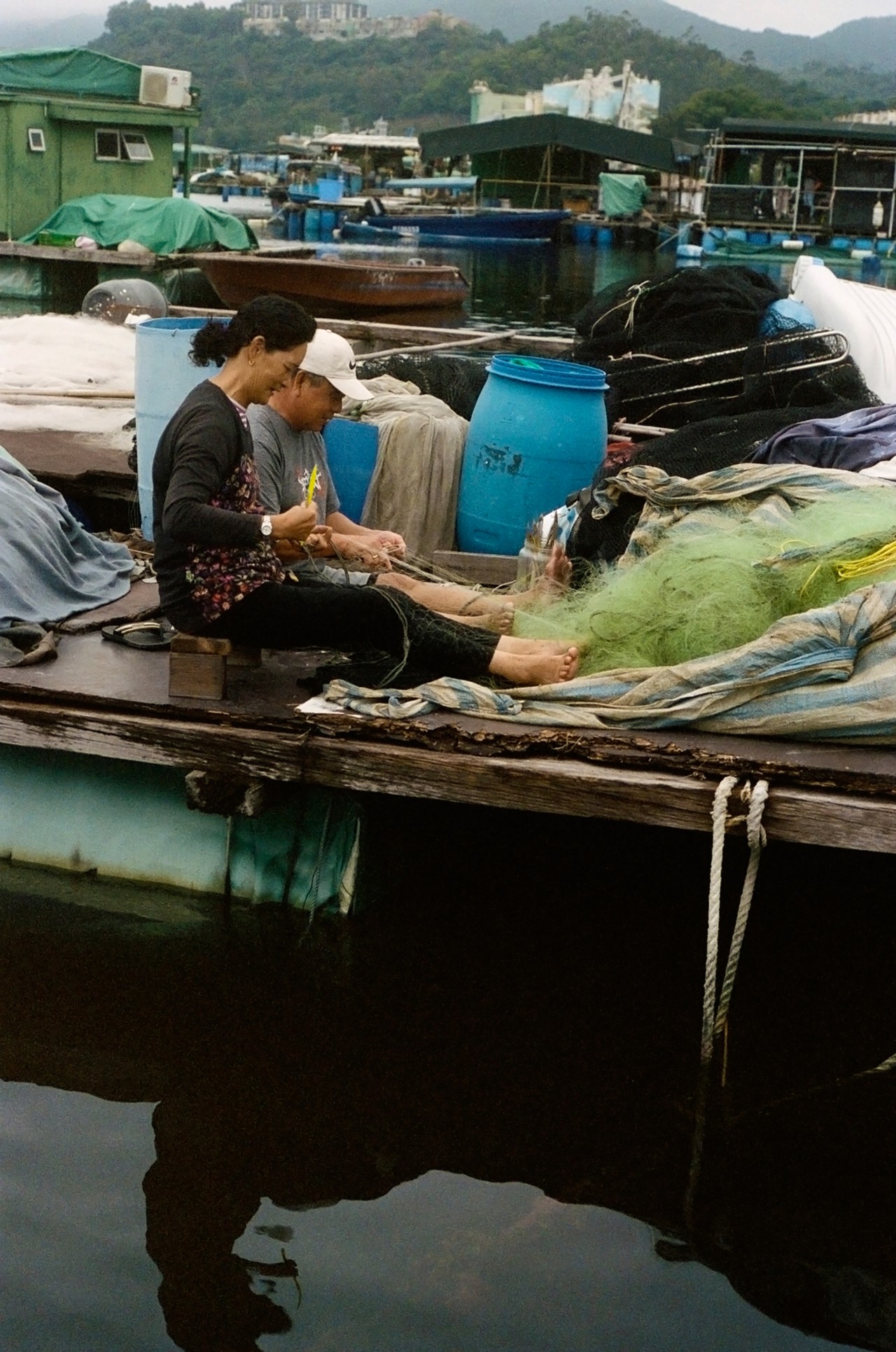 Two people sit on a boat in a fishing village, working on the food they caught.
