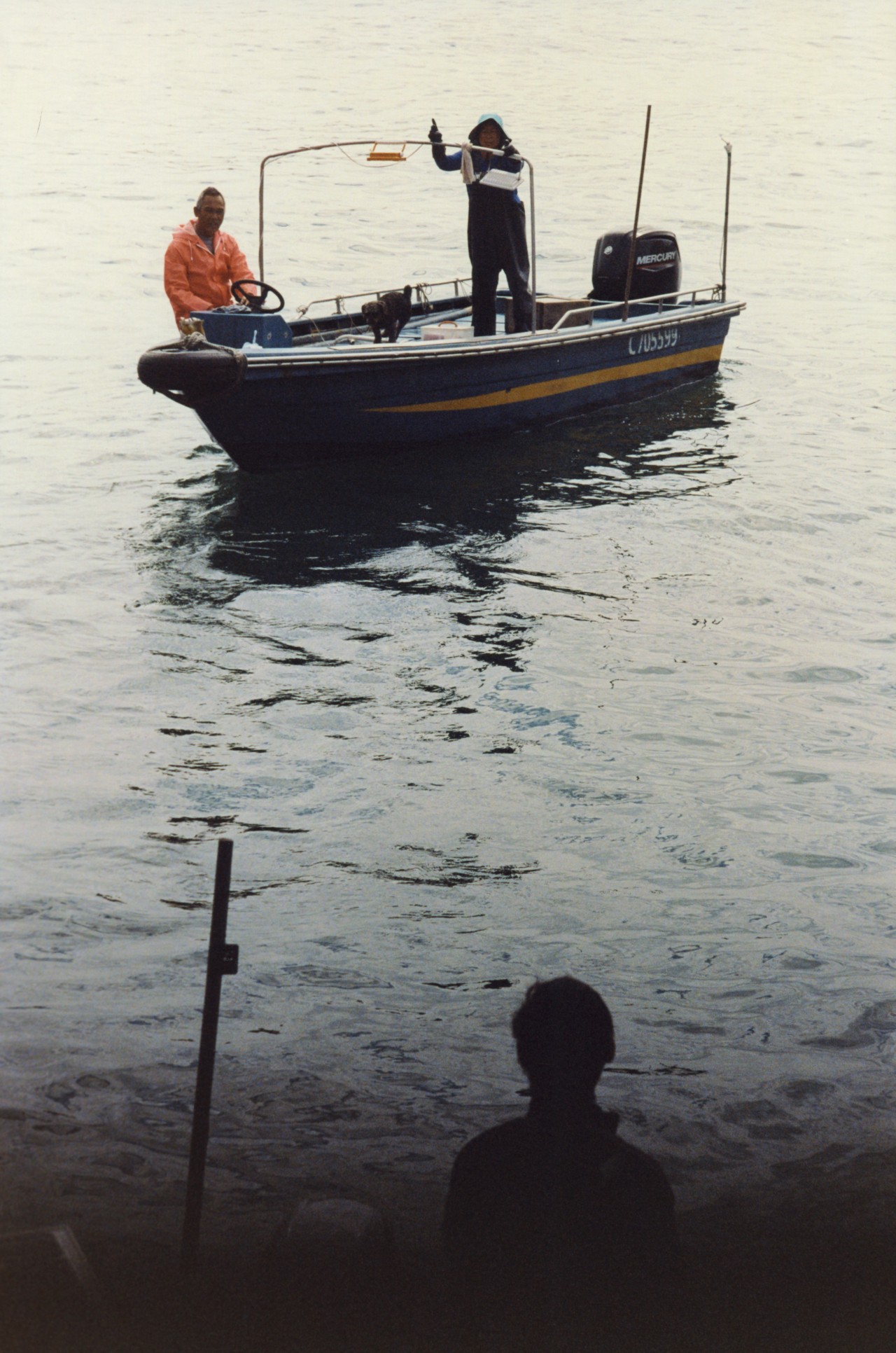 Two people stand in a small boat in a Hong Kong village.