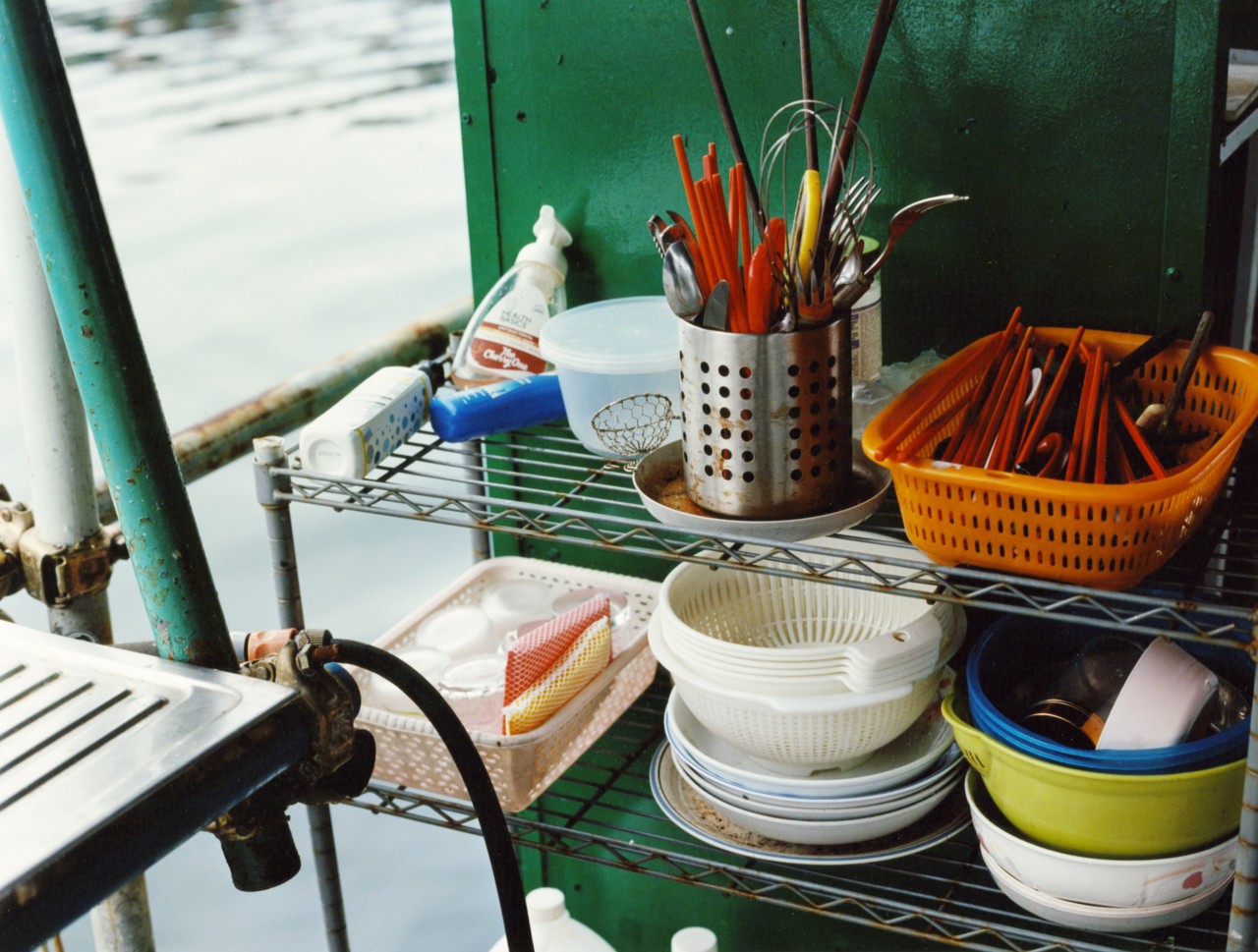 Several kitchen utensils sit on a shelf on a boat in a Hong Kong village.