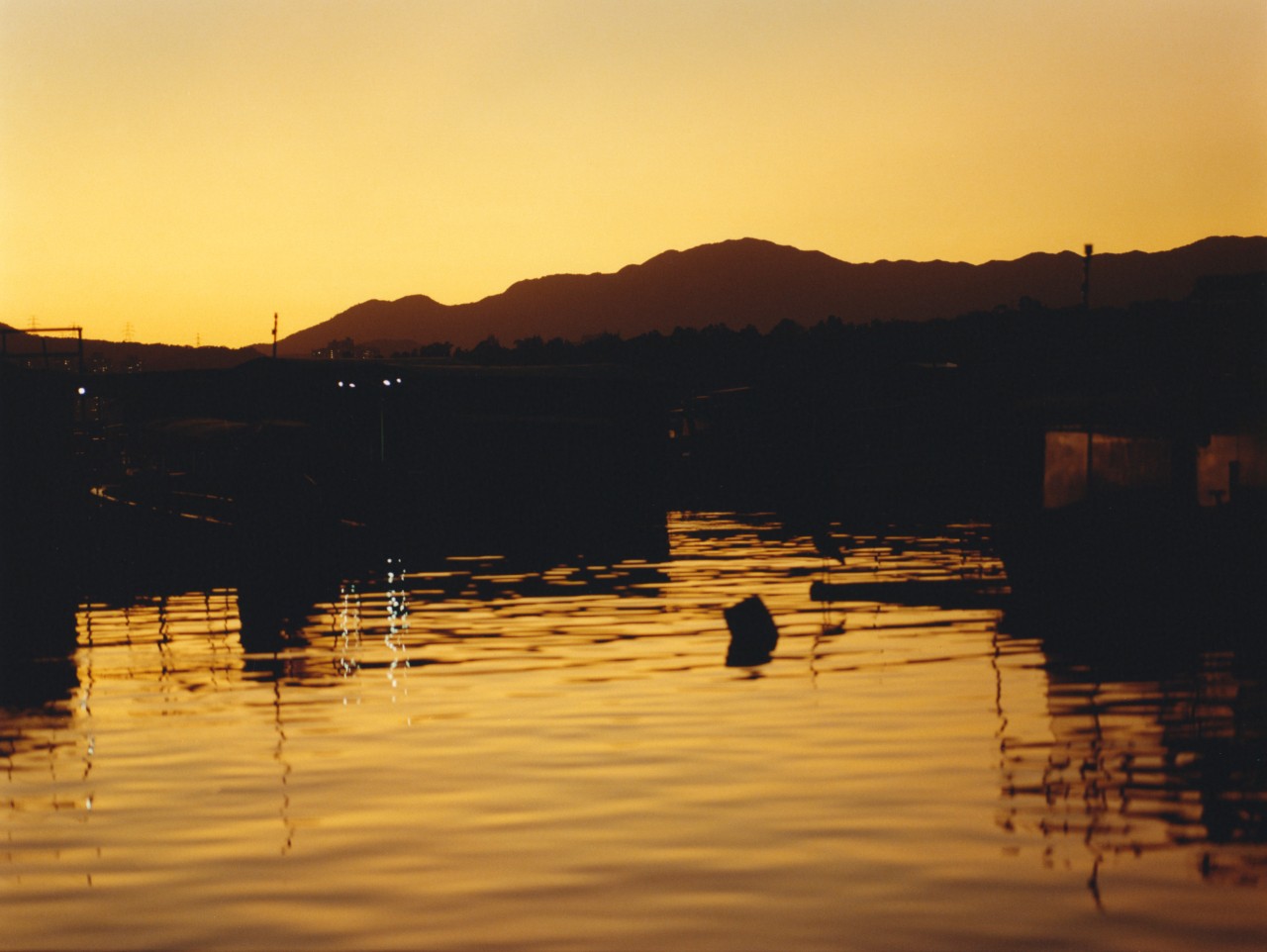 The sunlight reflects off a body of water during dusk with mountains in the background.