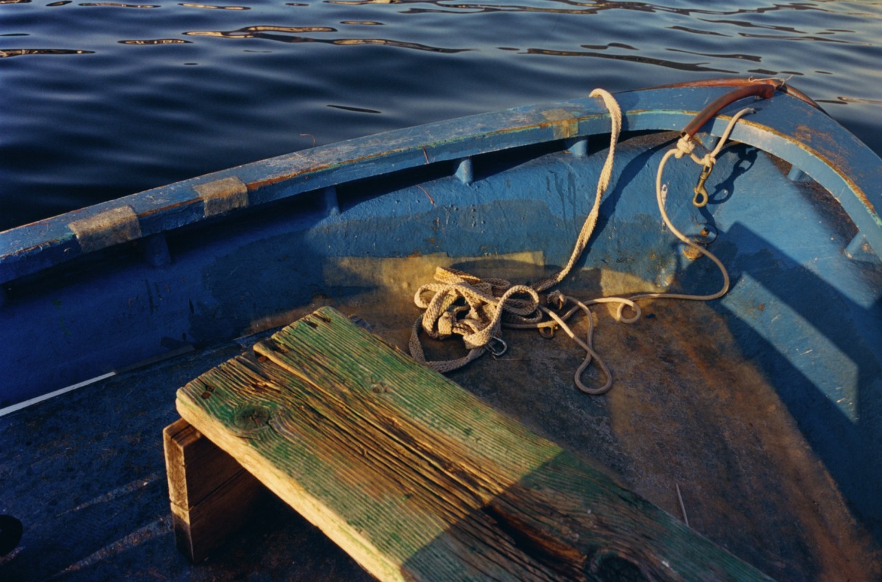 A slab of wood sits in a blue boat on the water in a Hong King village.