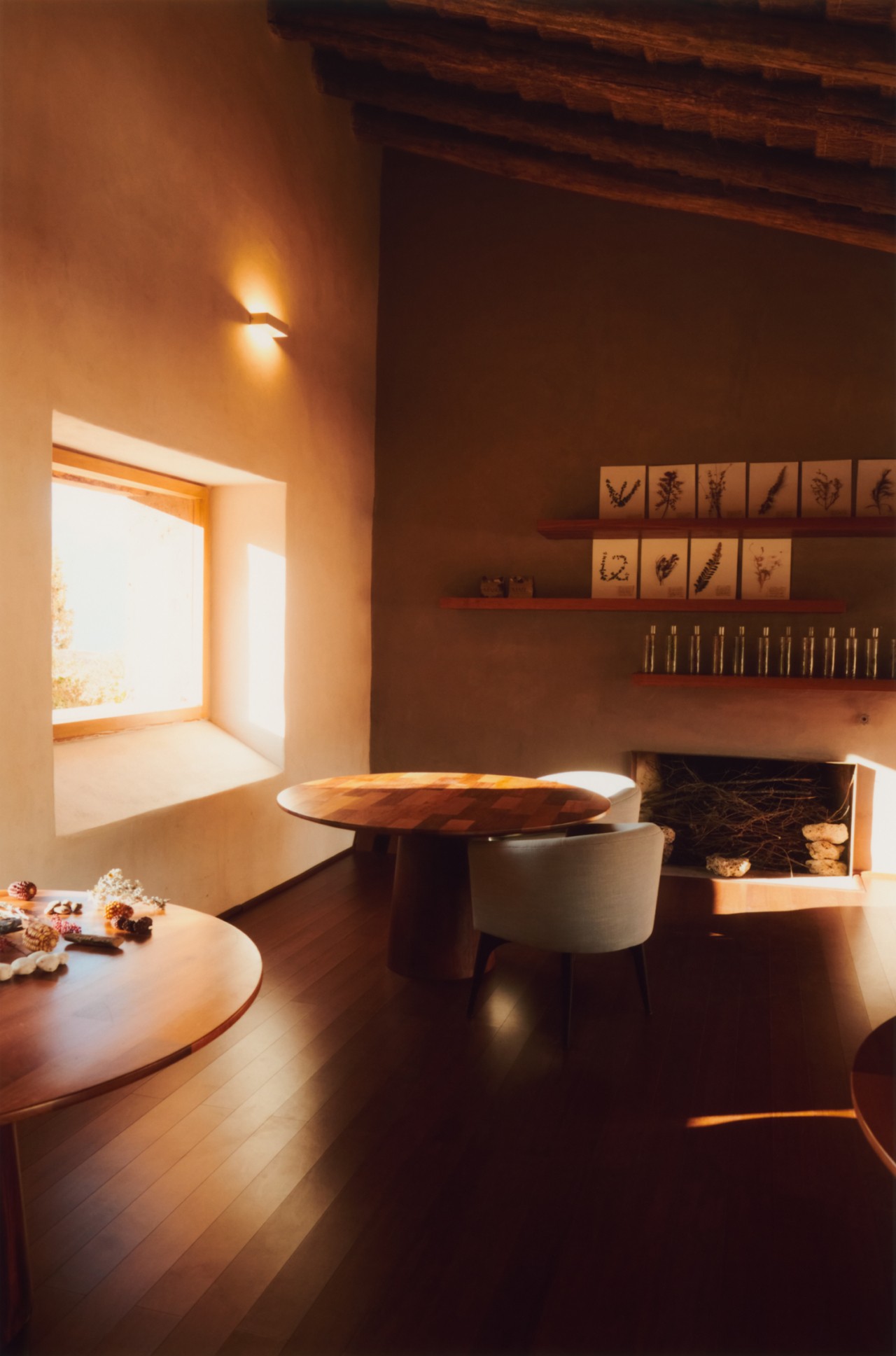 The inside of a living room with chairs, tables, and artwork. The sun is peeking through a large window to the left.
