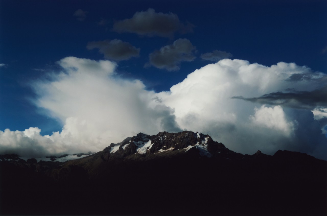 The clouds meet a large mountain in the distance.