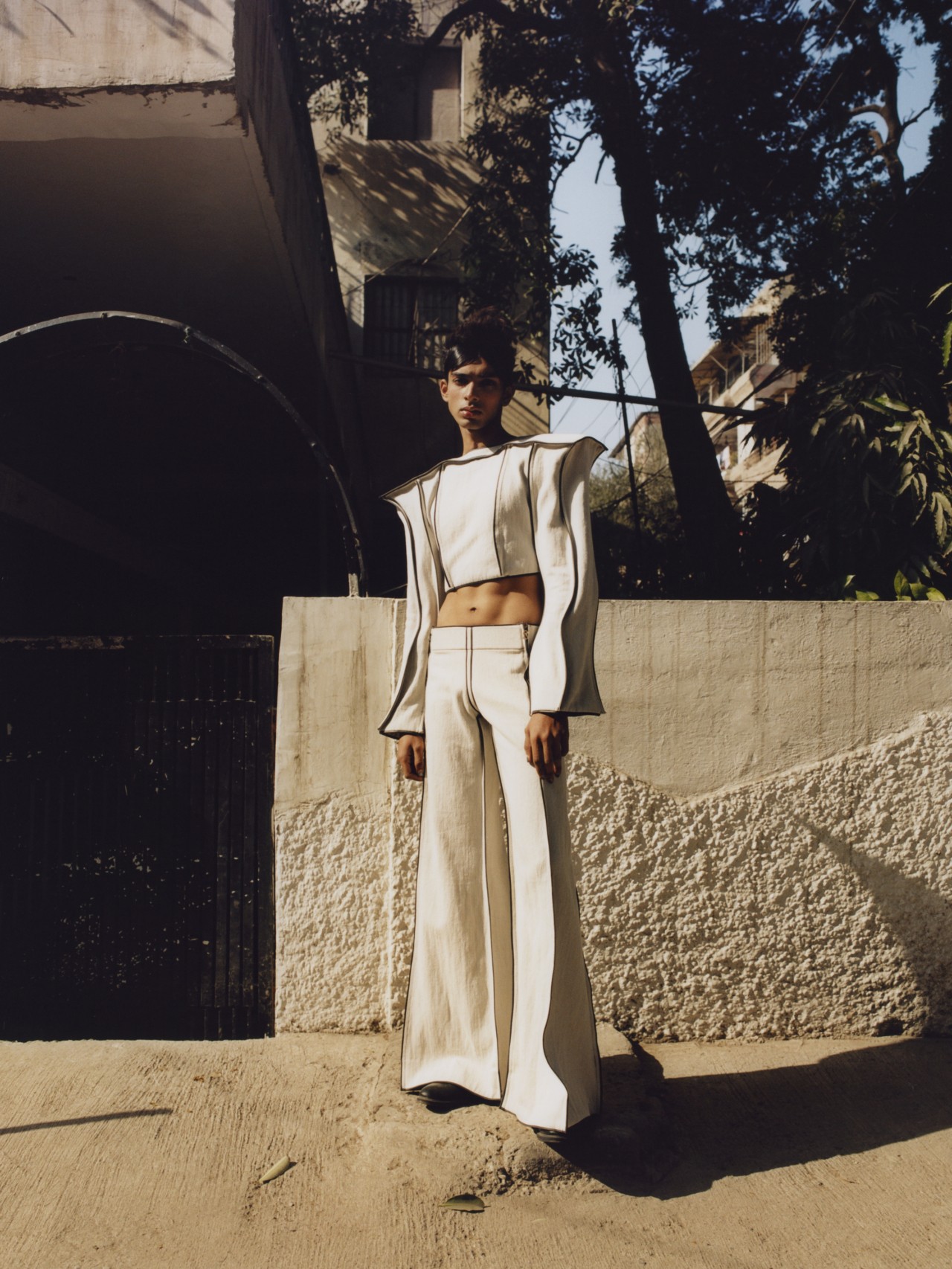A model wearing a two piece white pantsuit poses in front of a building.