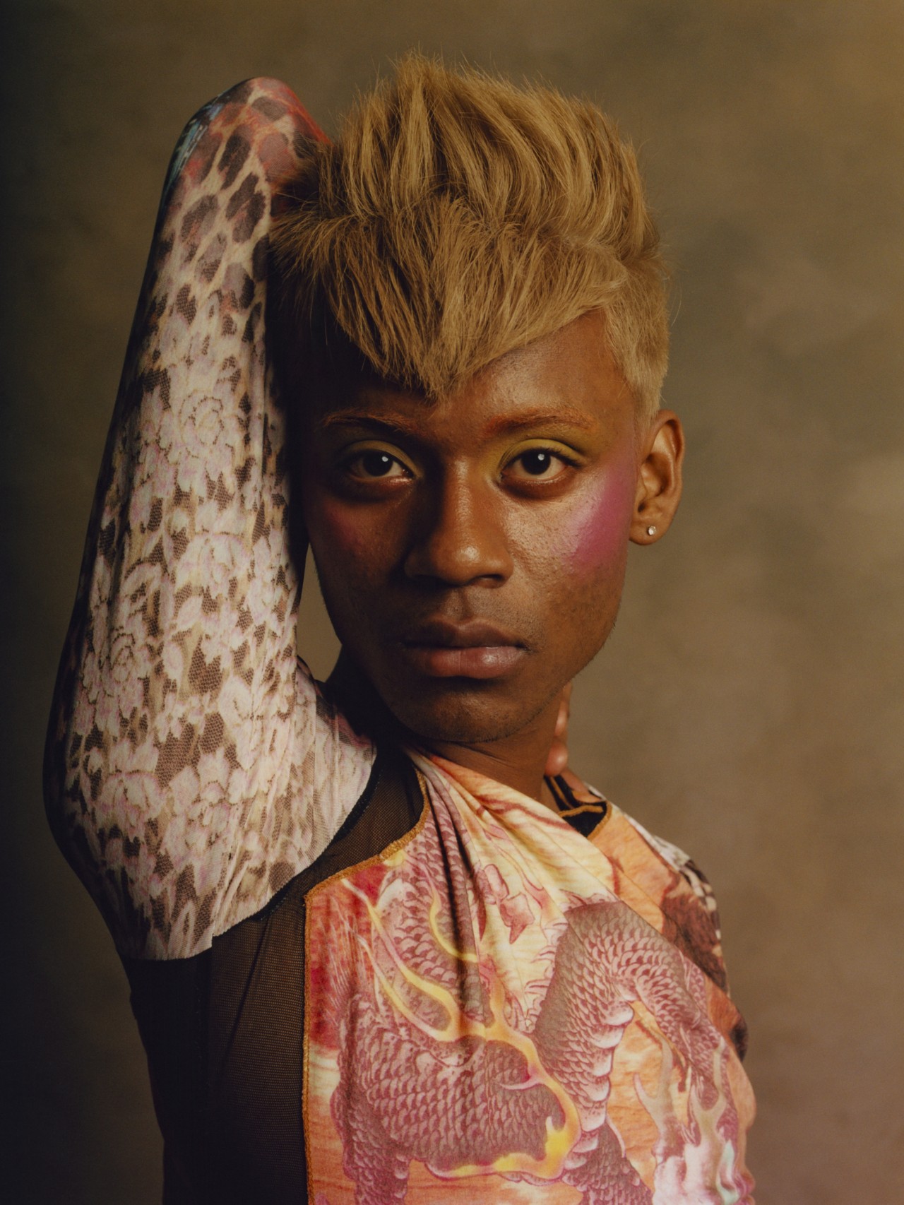 A model poses with a blonde pixie cut poses with their arm held up next to their head.