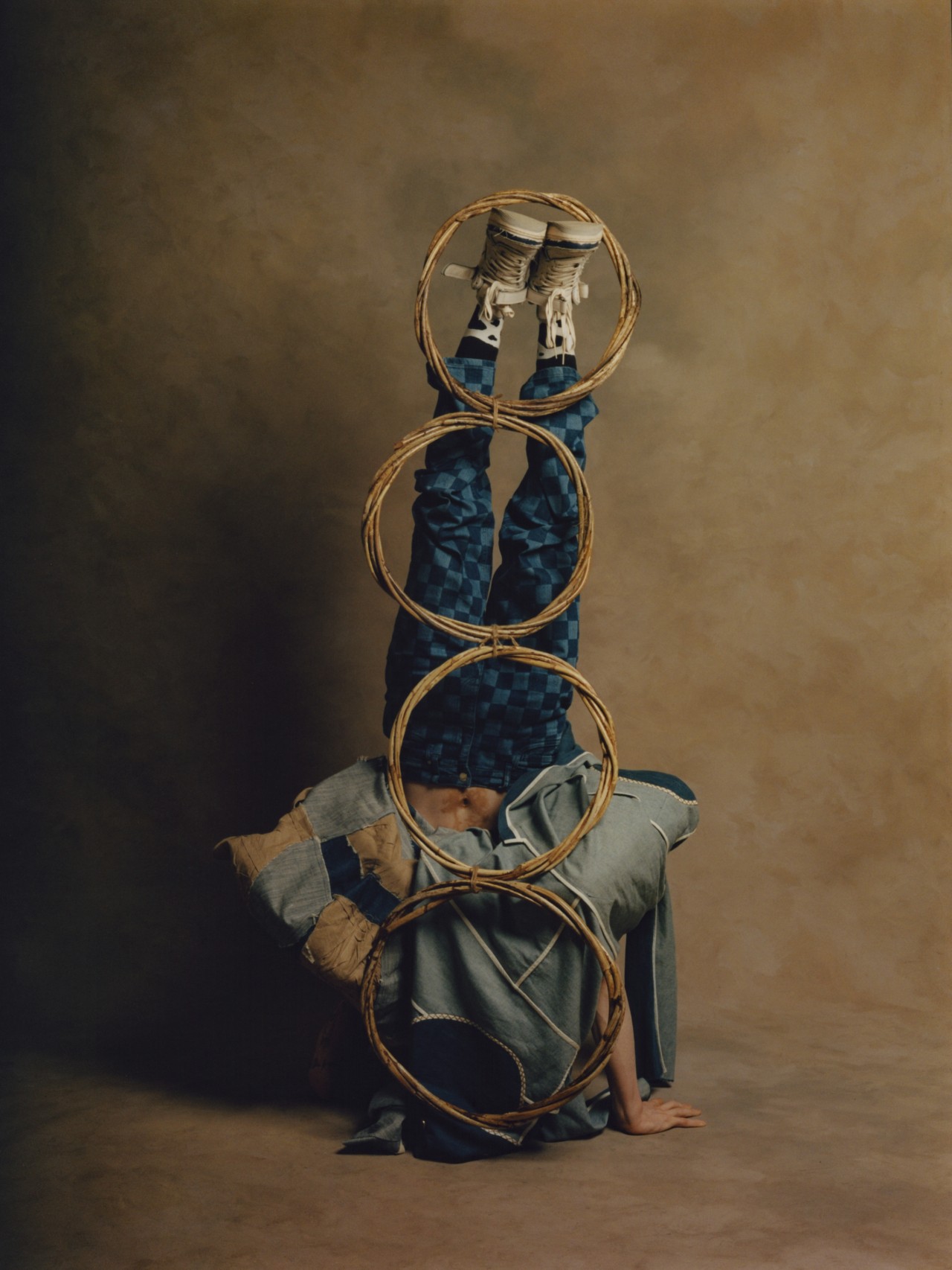 A model wearing a blue garment stands upside down on their hands, with four circular objects set up along their back.