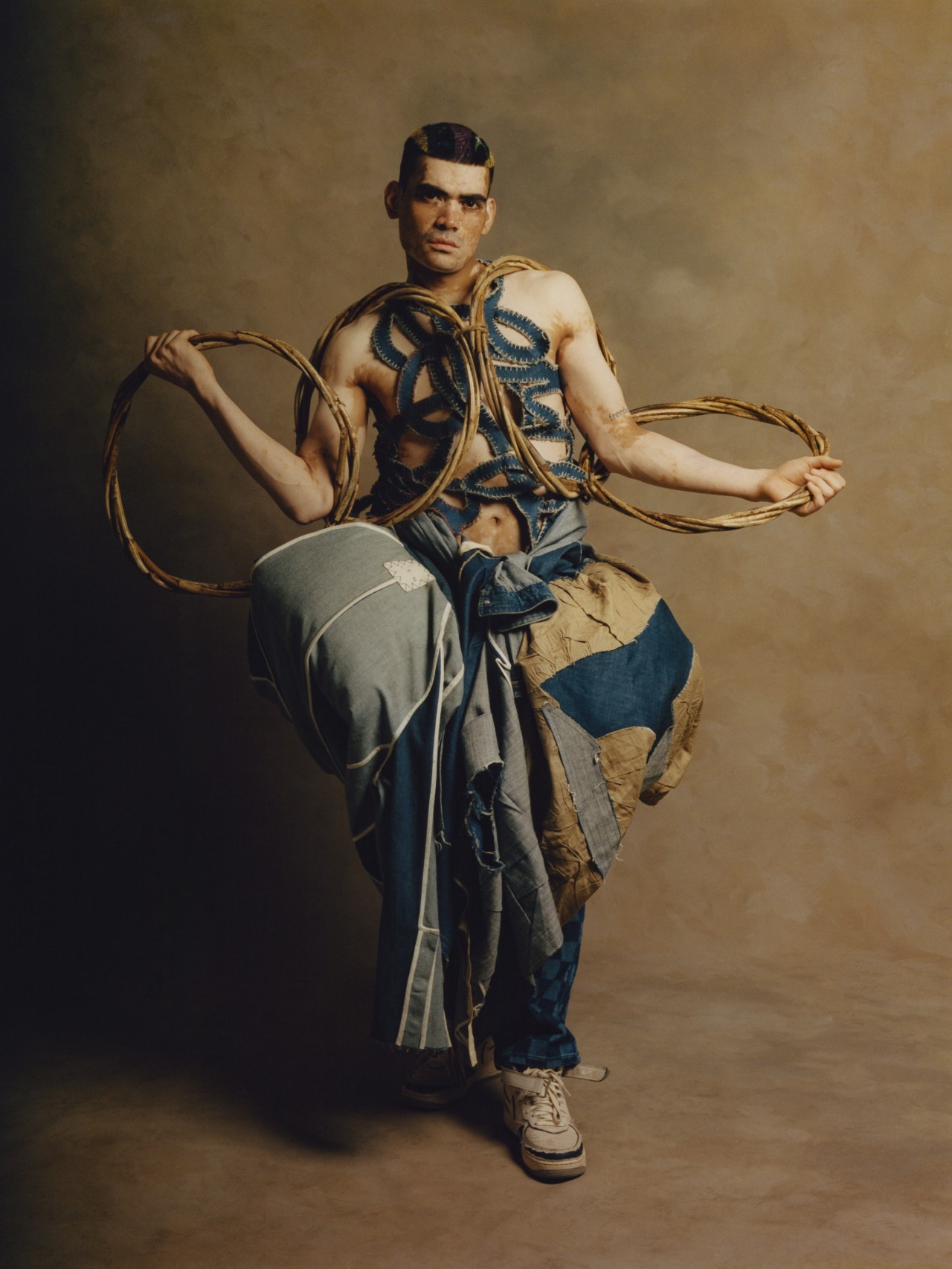 A model wearing a blue garment poses while holding a circular object in each hand.