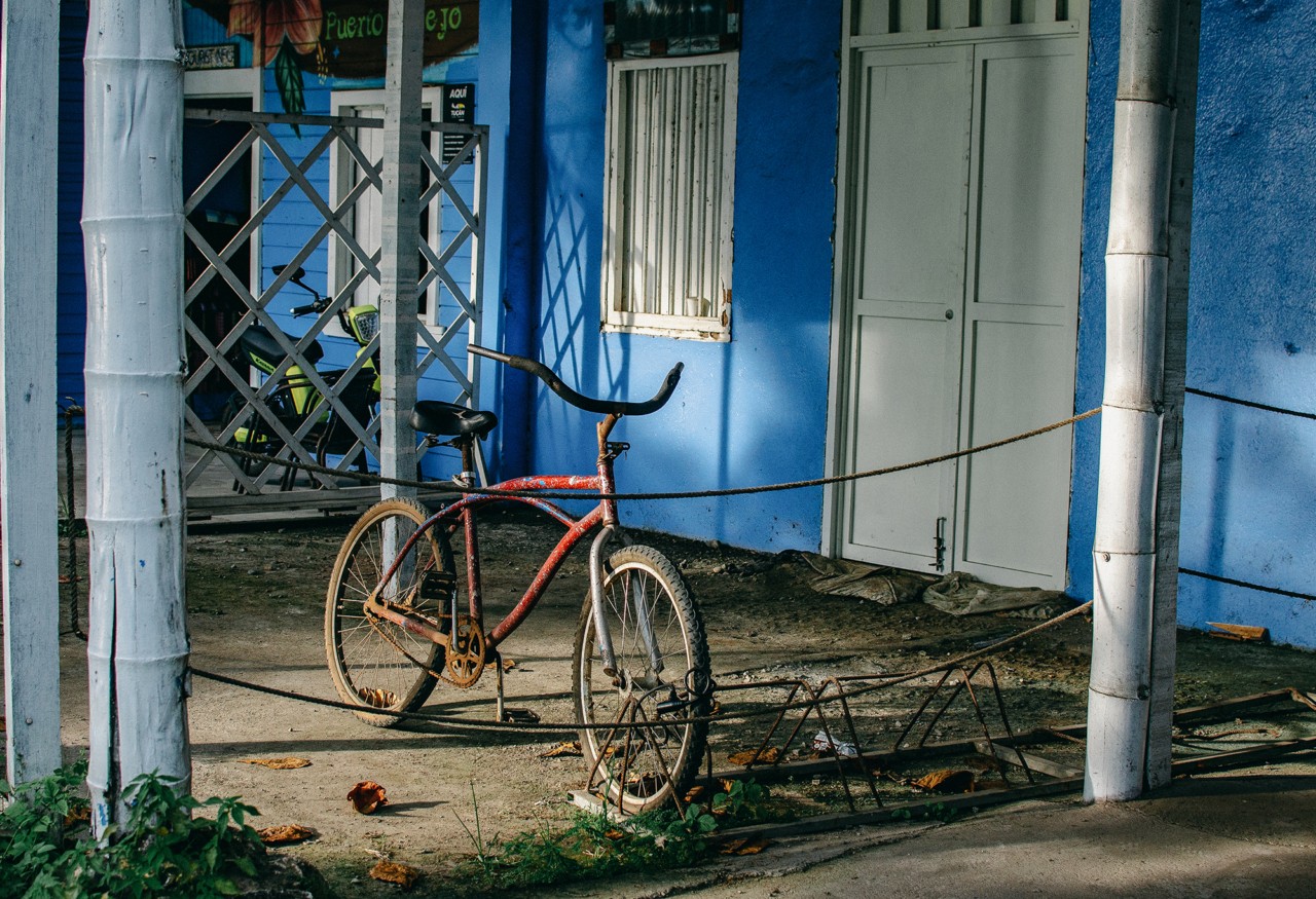 A red bike is parked outside a blue house in Puerto Viejo.