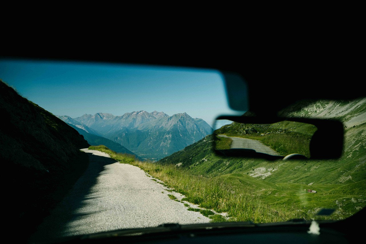 A view from the inside of a car that is driving along a road leading to a mountain top.