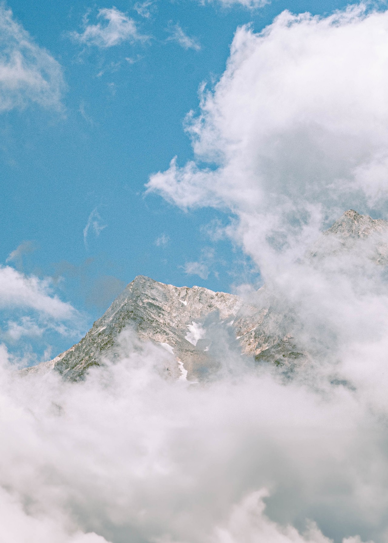 A rocky mountain peaks behind a sheet of stratus clouds high up in the sky.