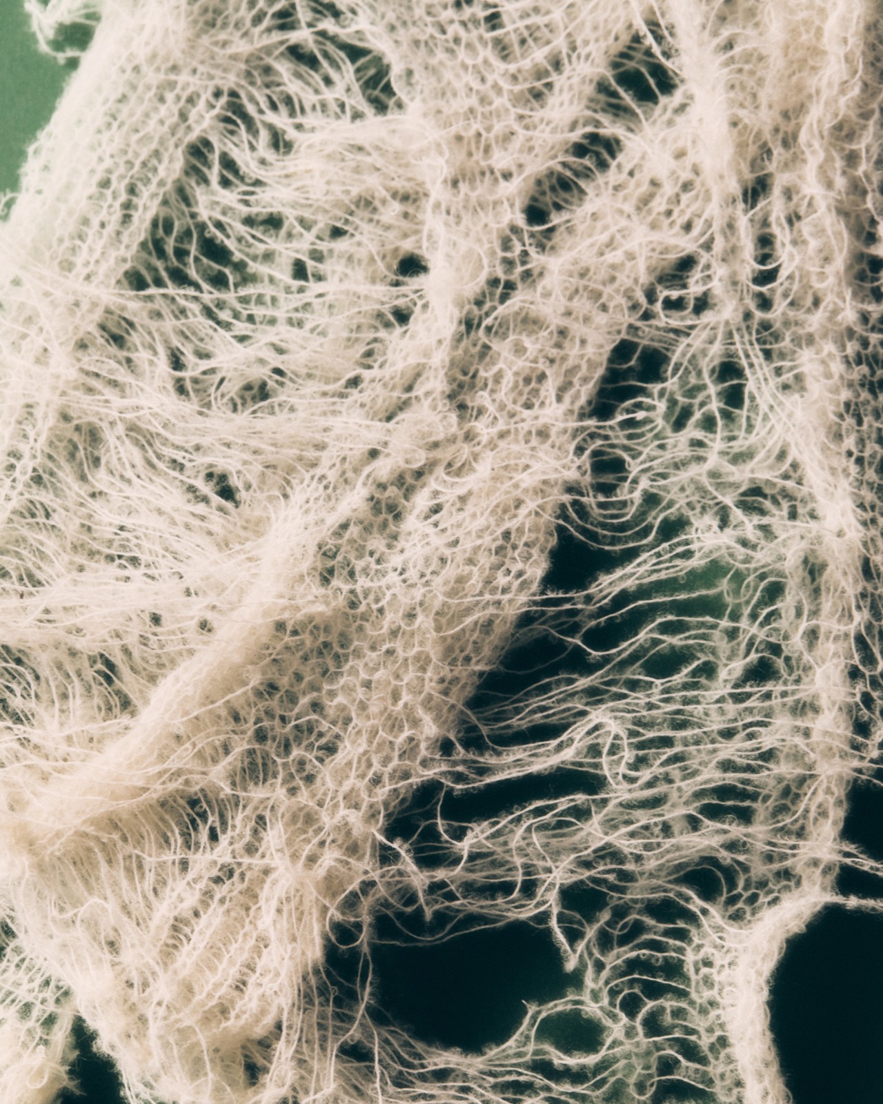 Frayed white wool lays on a green desk.
