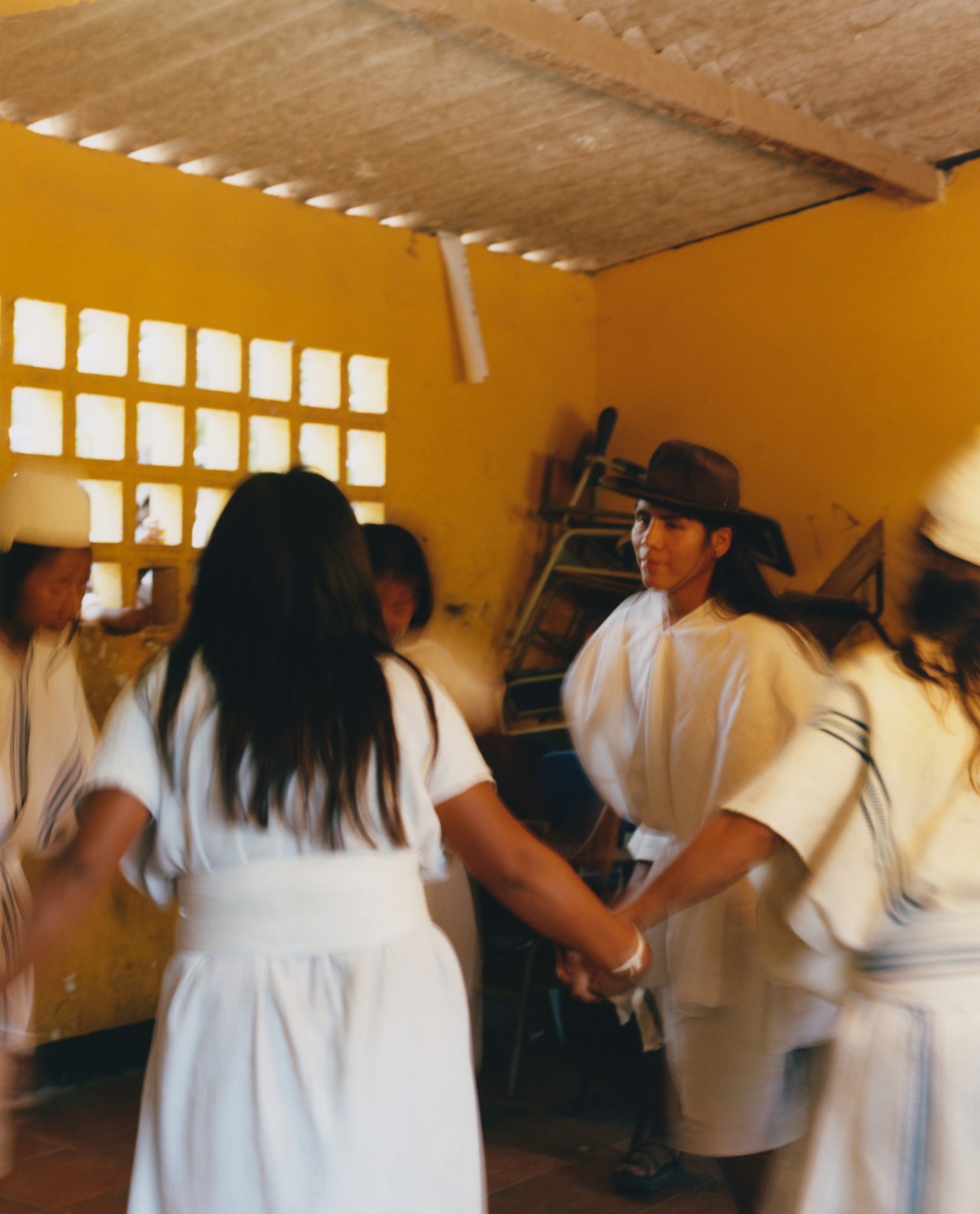 A group of Kogi people gather in a room to hold hands in a circle.