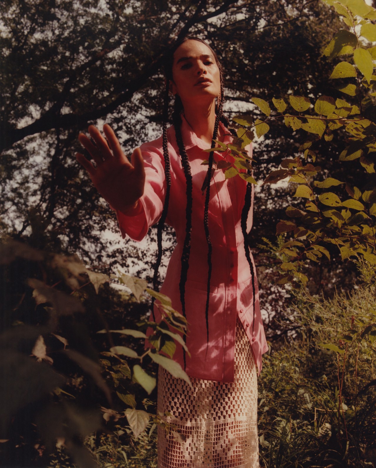 A model wearing a pink and white linen fabric outfit reaches toward the camera.