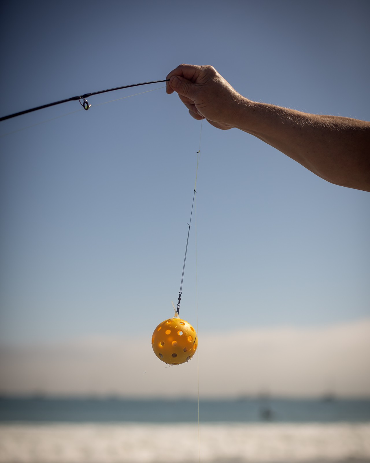 A person's arm is holding up a fishing hook with a orange plastic ball attached to the end.
