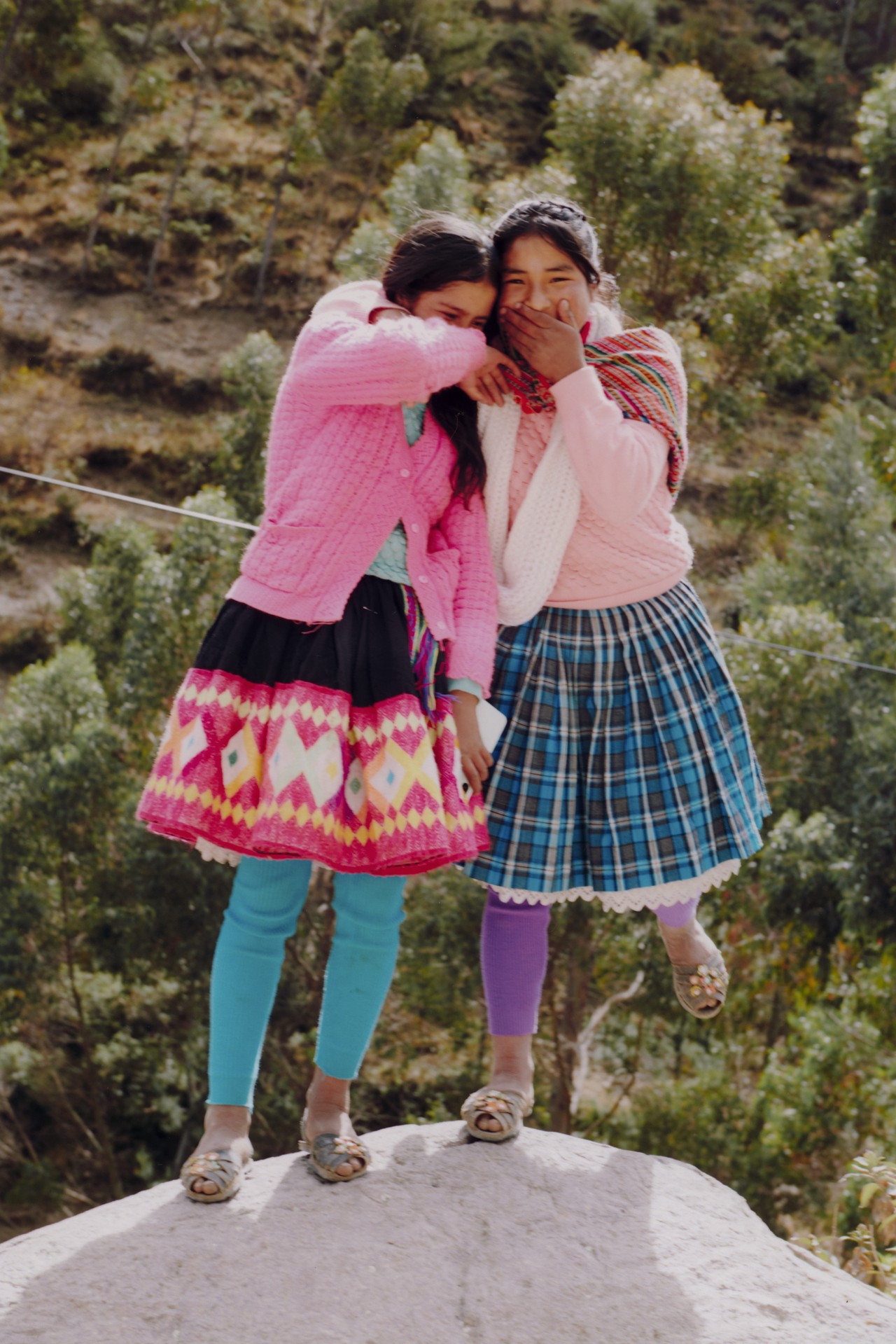 Two young girls from the Racchi community hug while standing on top of a rock in Cusco, Peru